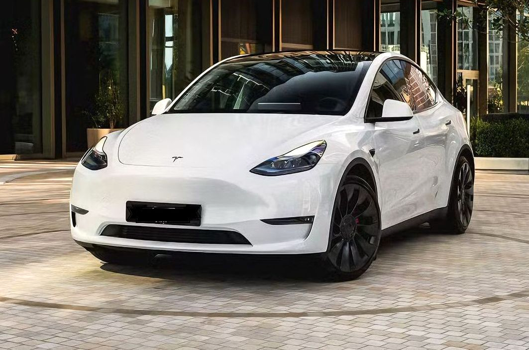 White Tesla Model Y parked outside a building with a black roof and dark wheels.