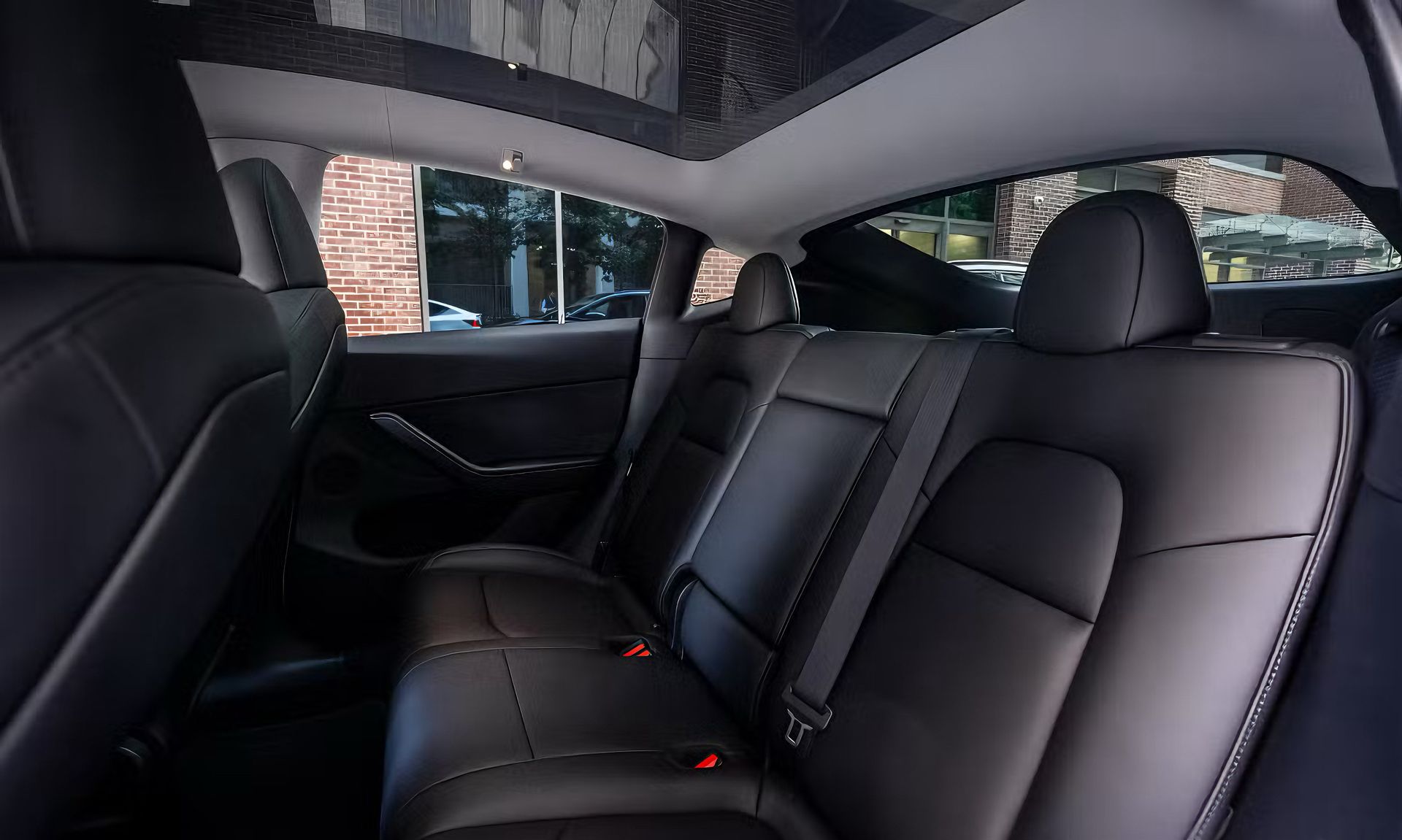 Black leather rear seats in a modern car interior with a panoramic sunroof and window view.