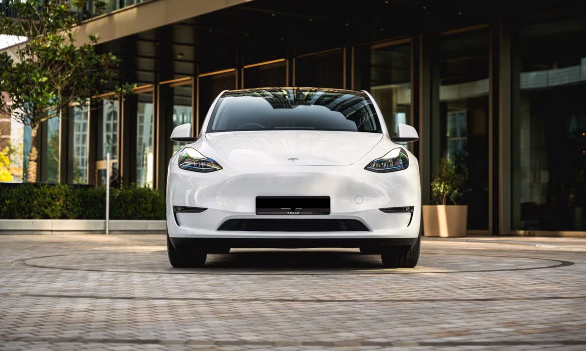White electric sedan parked in front of a modern building entrance