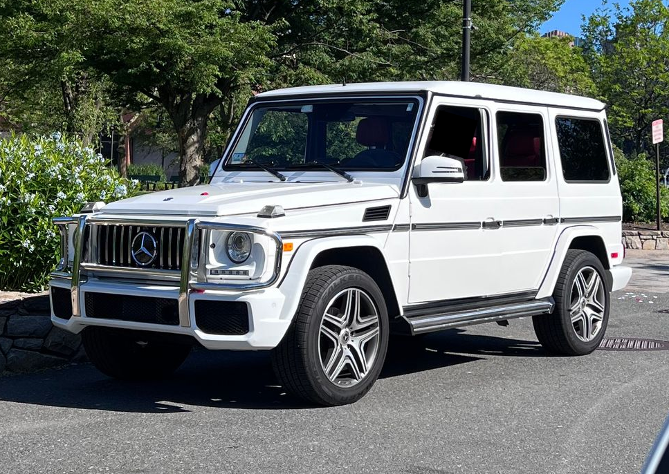 White Mercedes-Benz G-Wagon SUV parked on a rooftop with a city skyline in the background.
