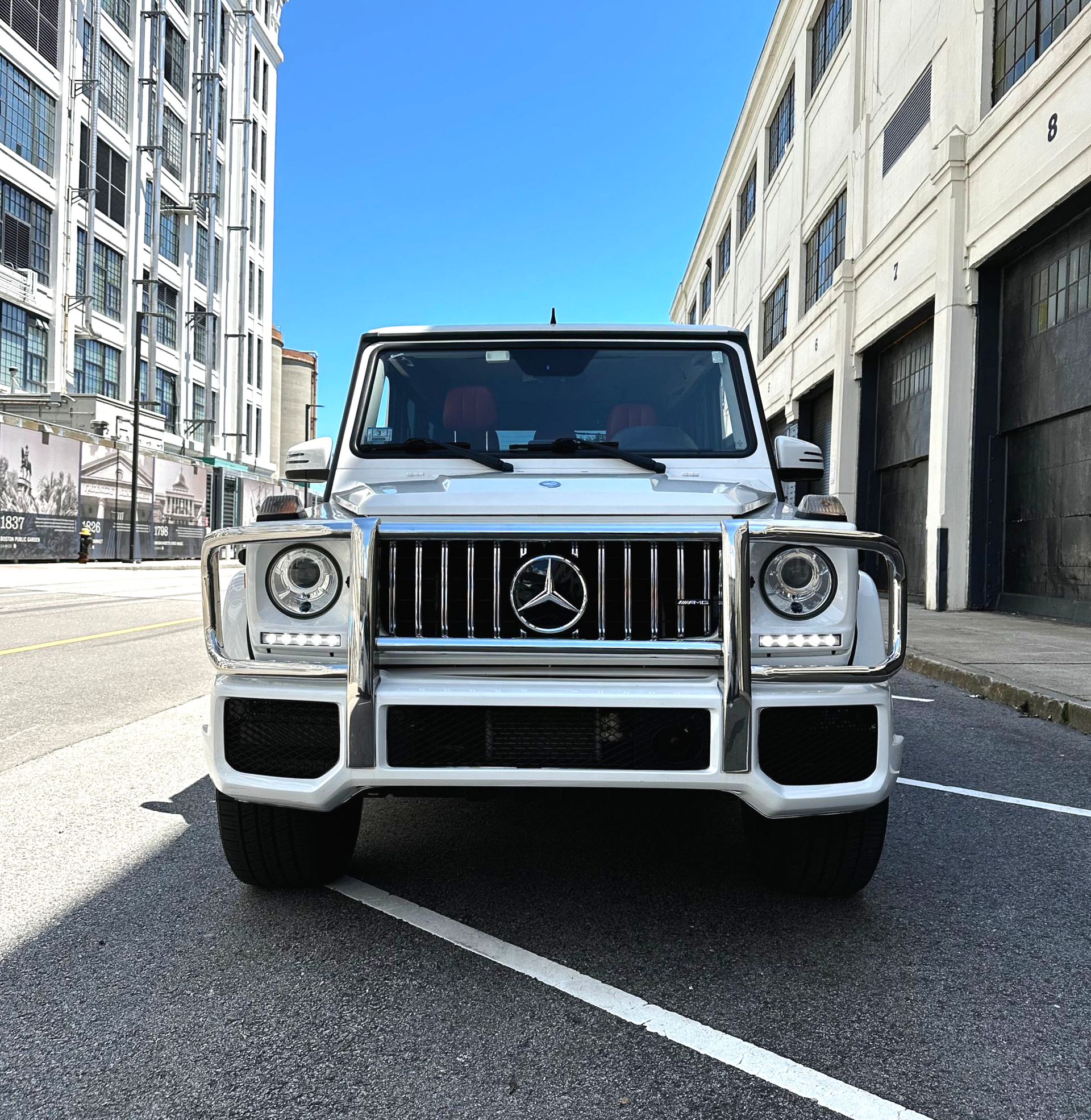 Front view of a white Mercedes-Benz G-Class on a city street between tall buildings