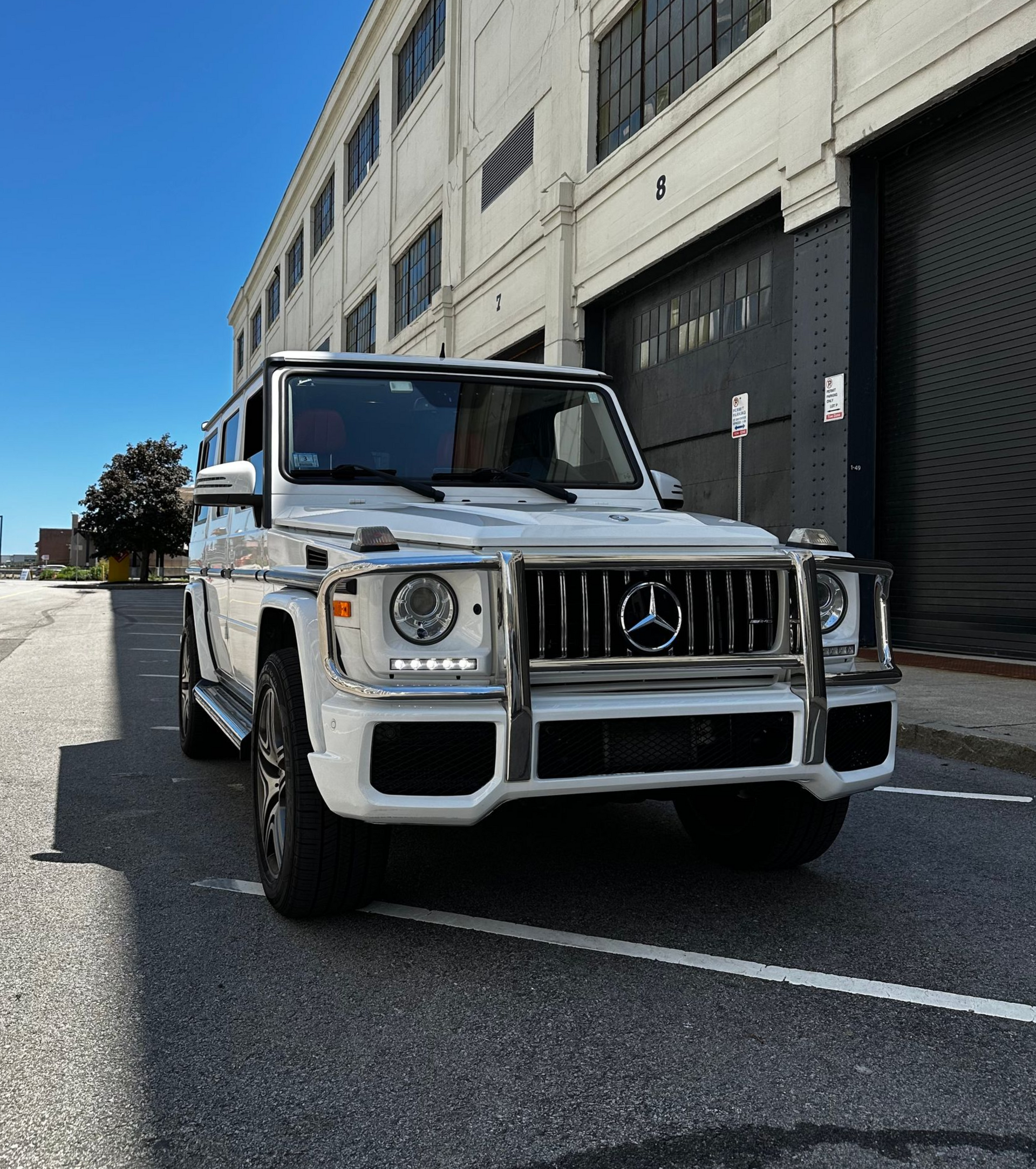 Silver Mercedes G-Class SUV parked on a sunny street beside a white building