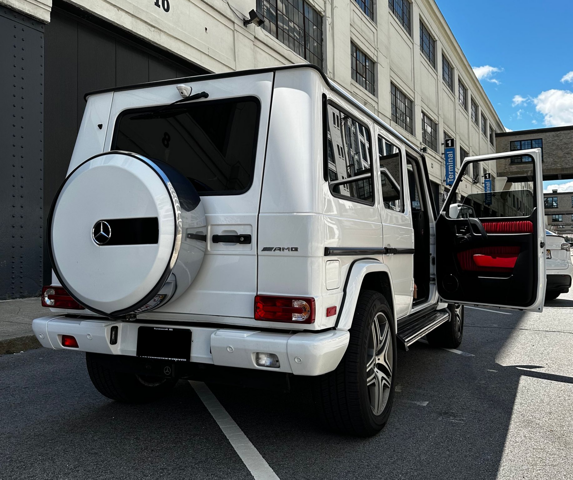 White Mercedes G-Class SUV parked outside a building, rear view with passenger door open.
