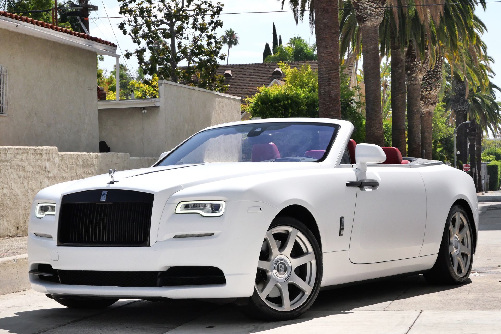 White Rolls Royce convertible parked on a street with palm trees.