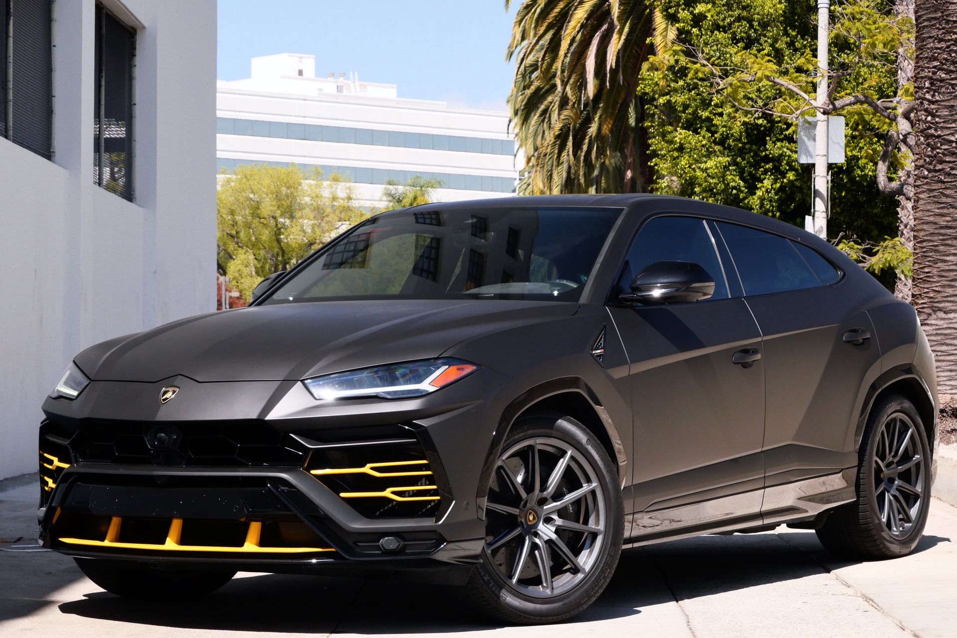 Matte gray Lamborghini Urus SUV with yellow accents parked in front of a white building.