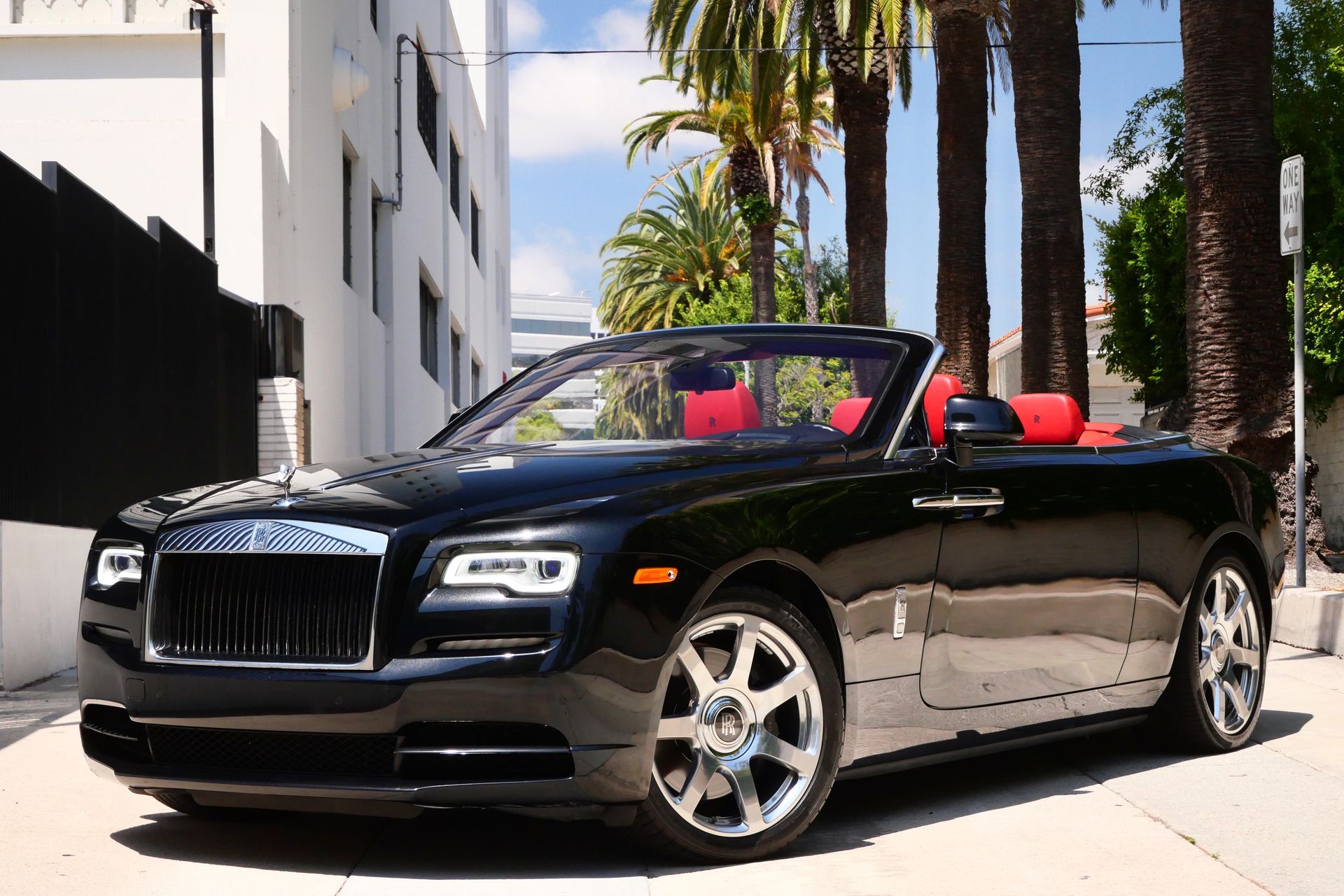 Black Rolls-Royce convertible with red interior parked on a street with palm trees.