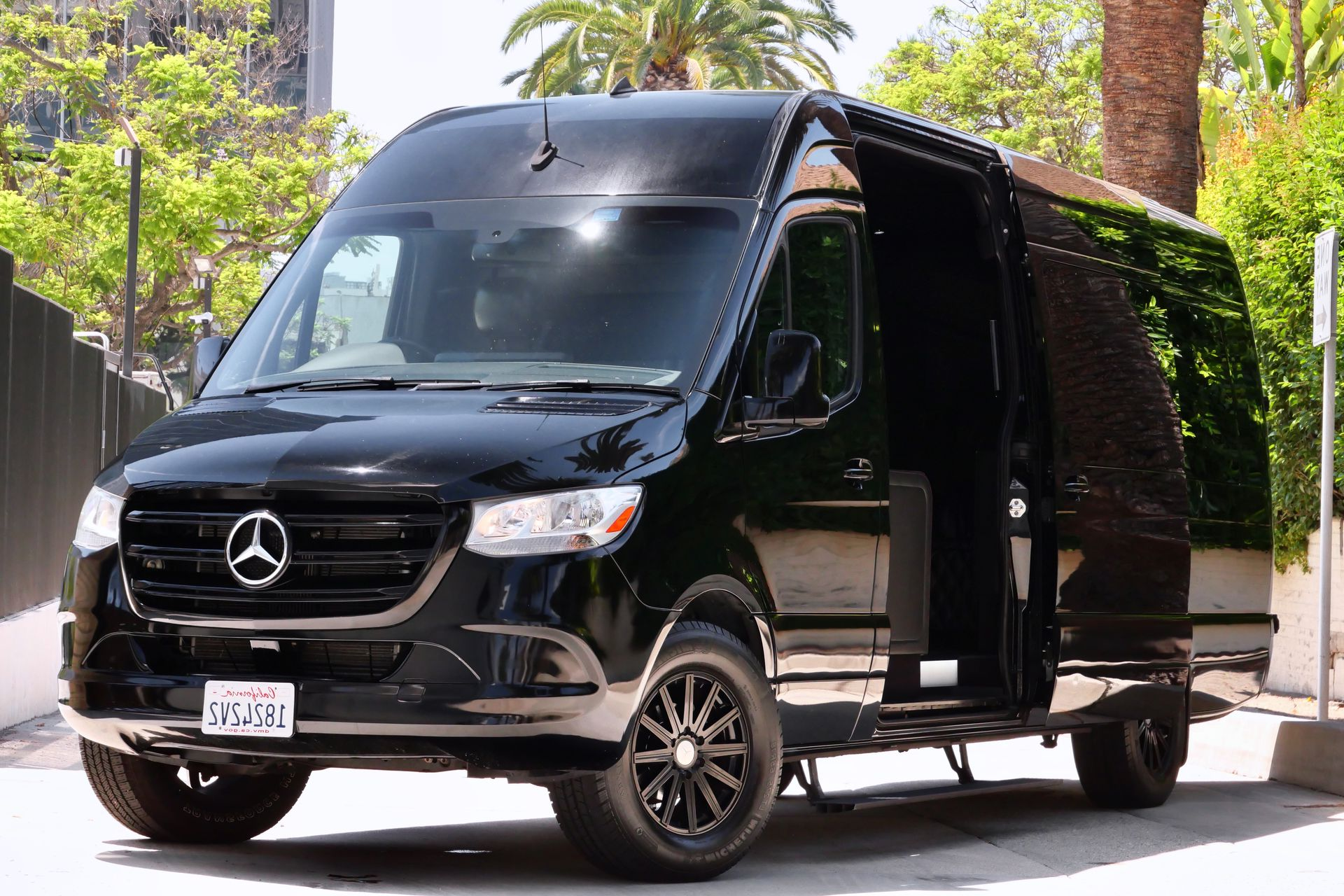 Black Mercedes Sprinter van with open sliding door. Parked outdoors.