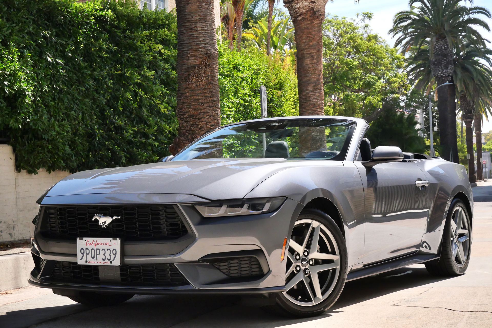 Gray convertible Ford Mustang parked on a street with palm trees.