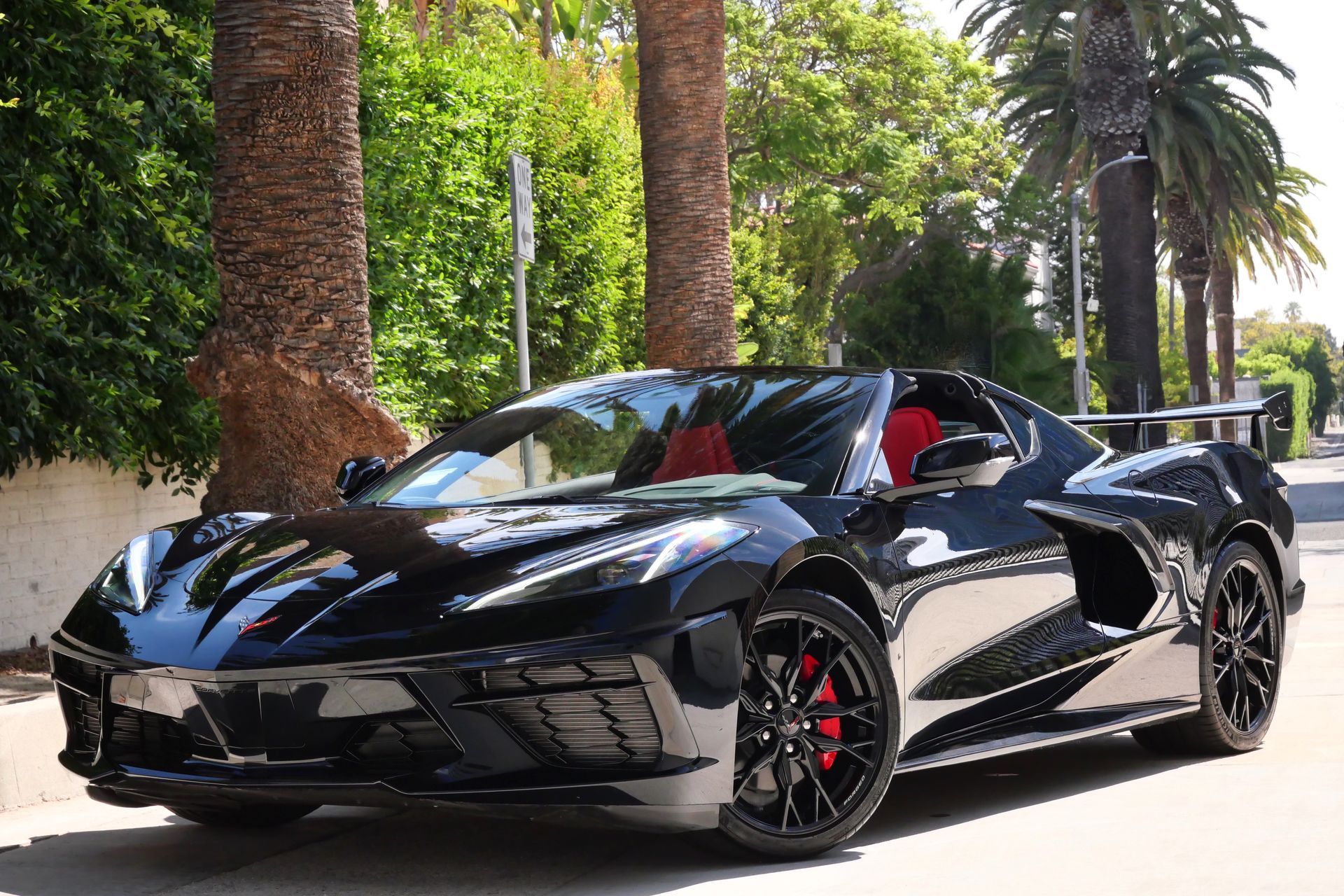 Black Corvette convertible with red interior parked on a street lined with palm trees.