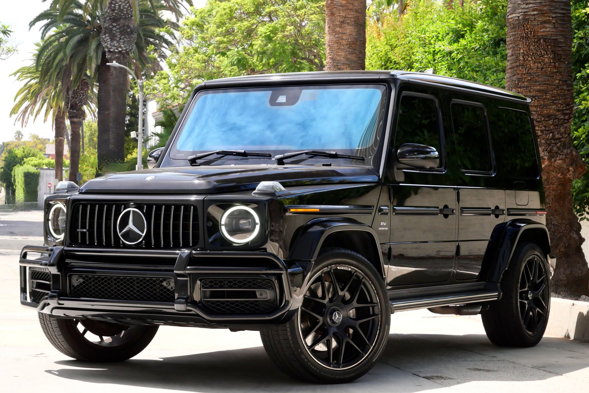 Black Mercedes-Benz G-Class SUV parked on a city street with palm trees in the background.