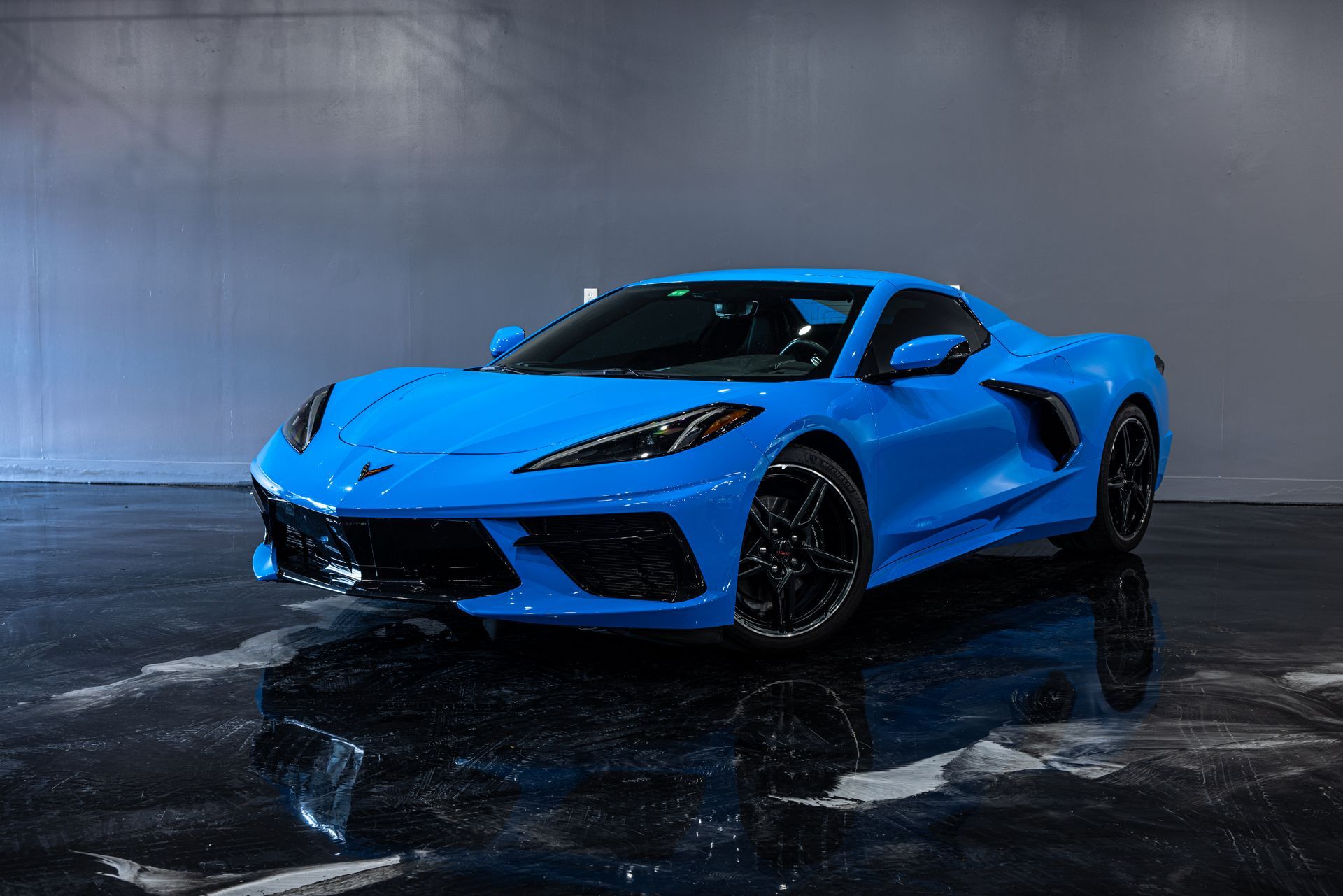 Blue Corvette sports car in a dark studio with reflective flooring.