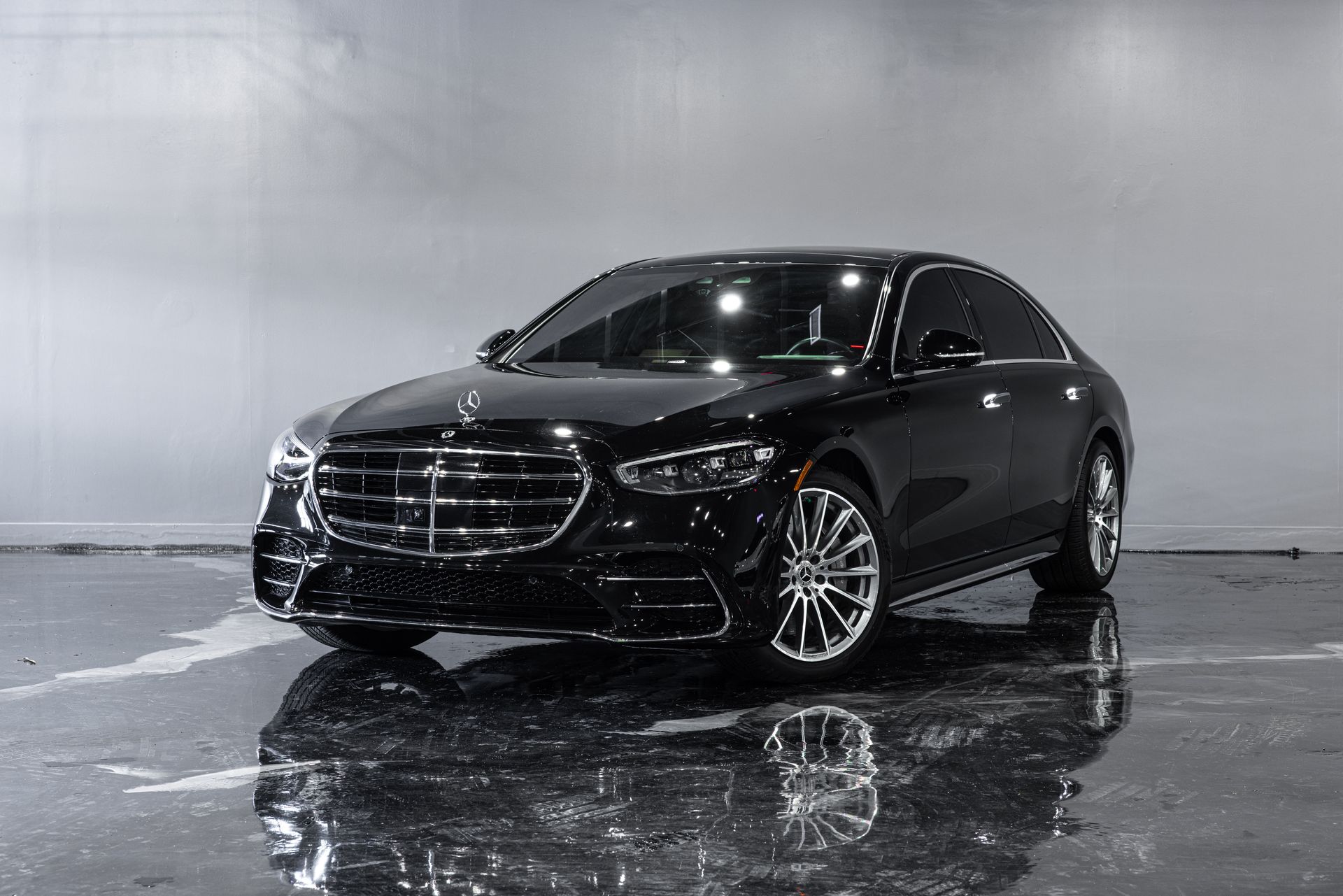 Black Mercedes-Benz sedan on a wet, reflective floor; indoor setting.