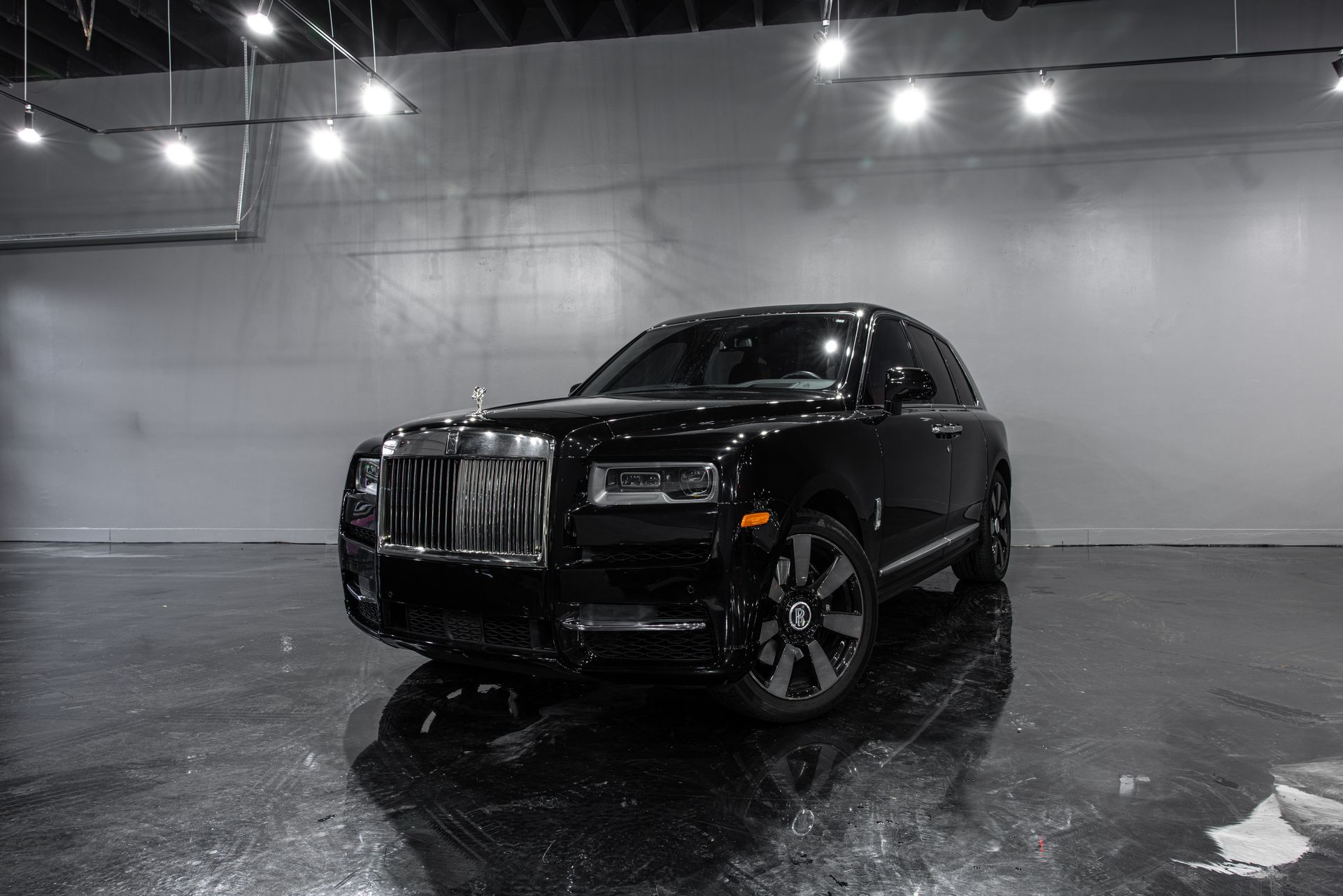 Black Rolls Royce Cullinan SUV parked inside a showroom with a reflective floor.