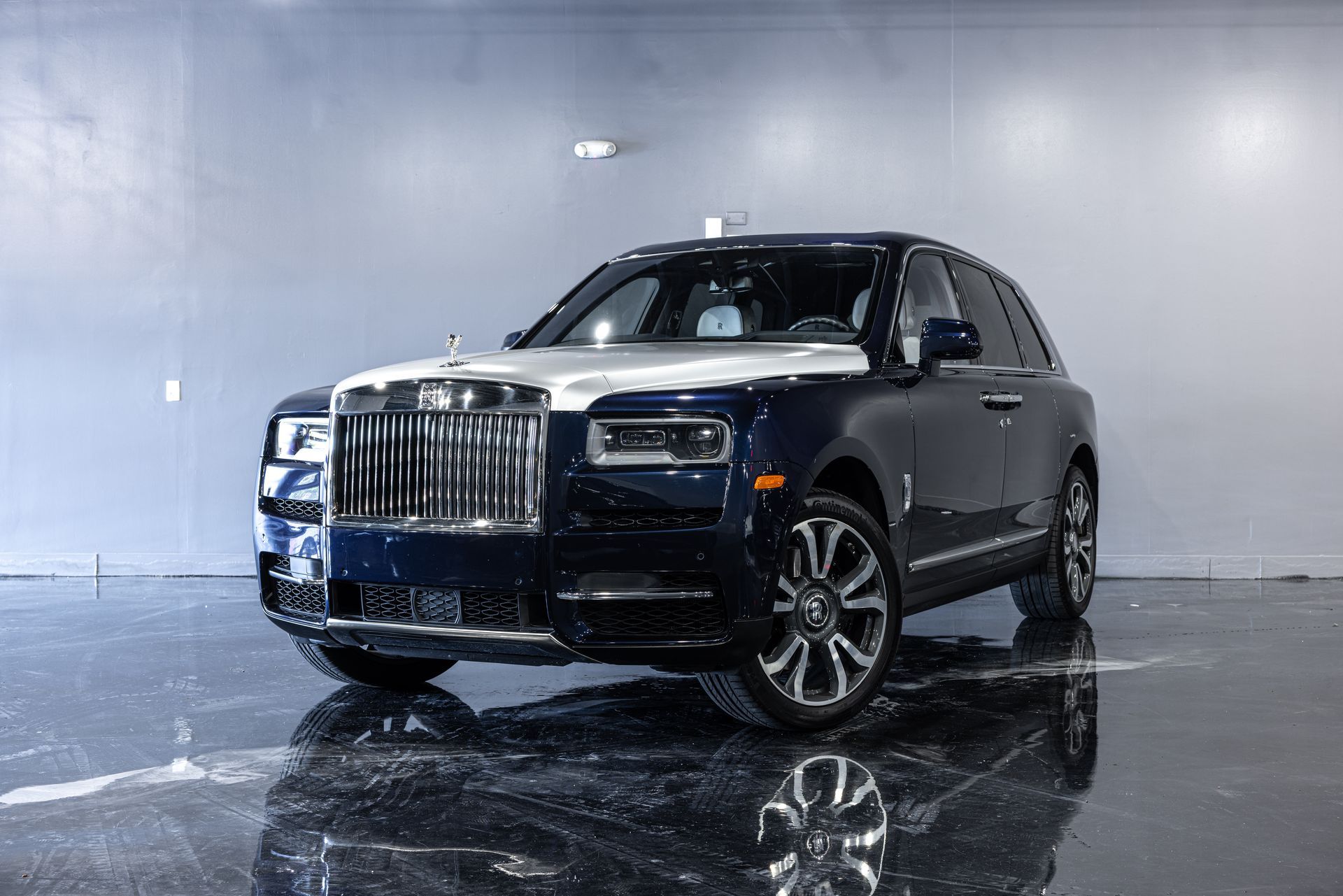 Blue and white Rolls-Royce Cullinan SUV parked in a studio with a reflective floor.