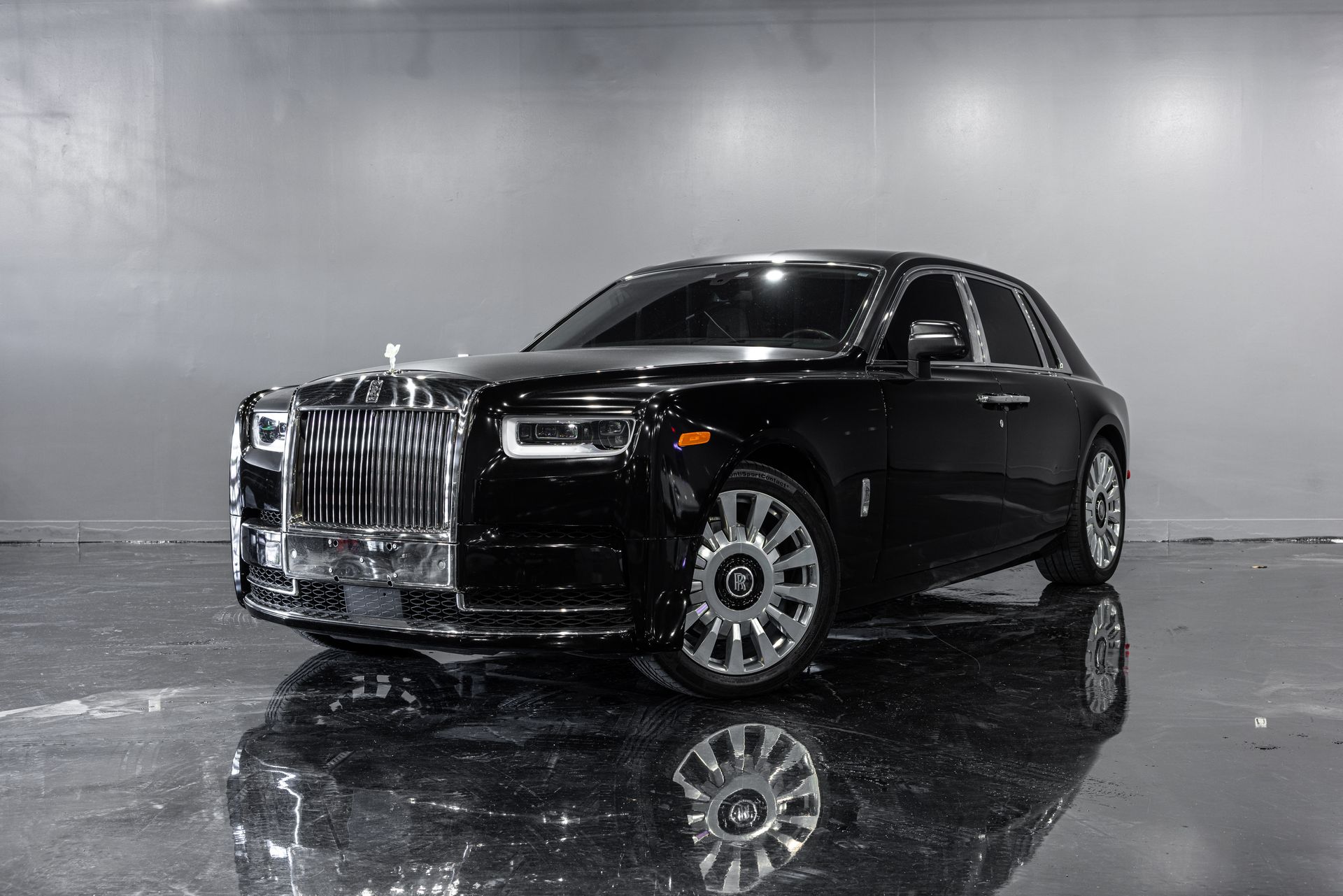 Black Rolls-Royce Phantom luxury car with silver grille, parked on wet pavement.