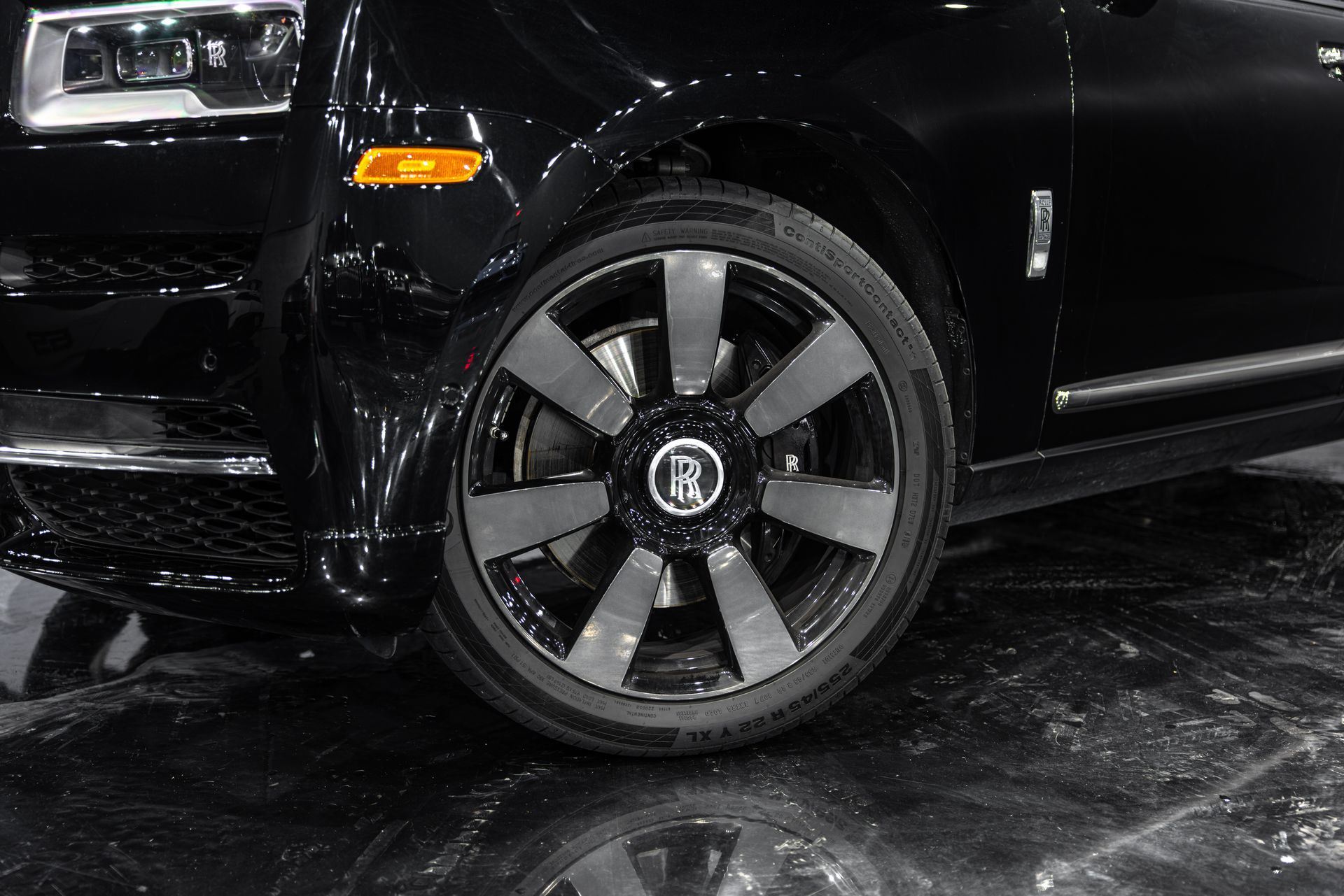Close-up of a black car’s front wheel with dark alloy rim on a shiny floor.