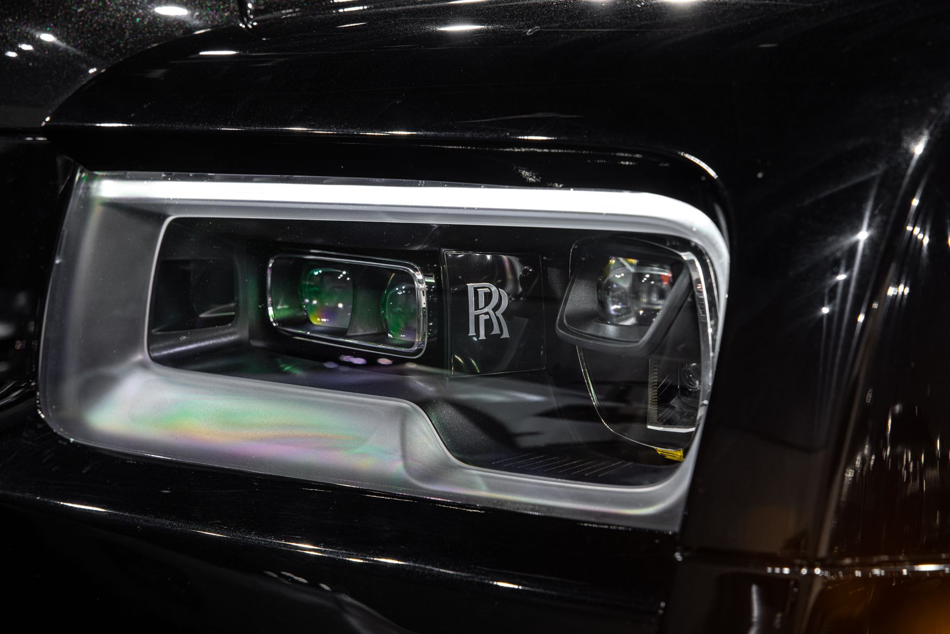 Close-up of a black Rolls-Royce headlight with chrome trim and a glowing LED accent