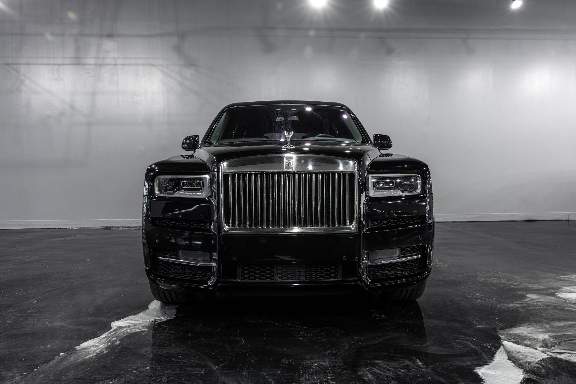 Front view of a black Rolls-Royce in a dim showroom, with a wet reflective floor.