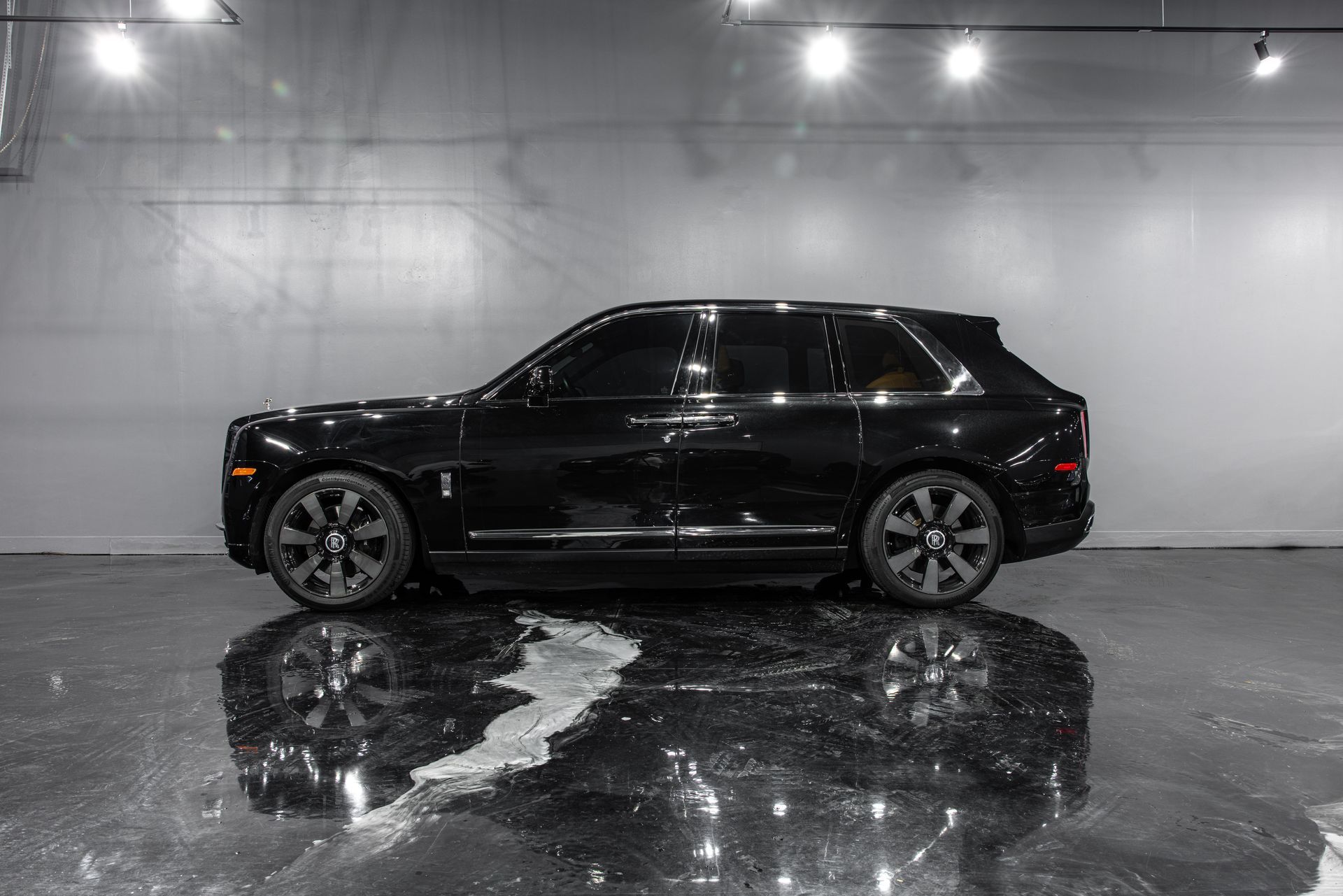 Black SUV in a showroom or garage, side view on a glossy wet floor with reflections