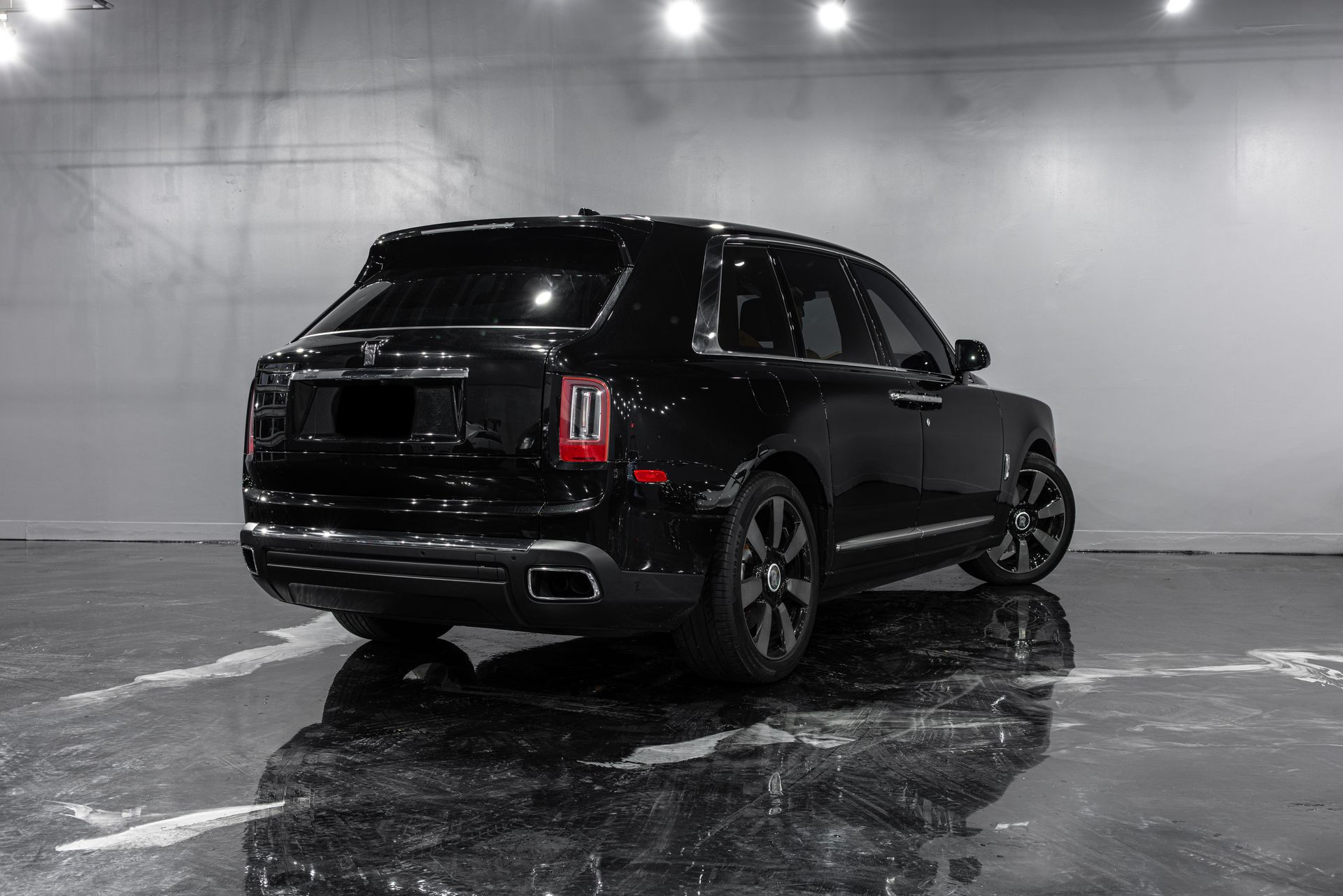 Black SUV in a showroom, viewed from the rear on a wet reflective floor.
