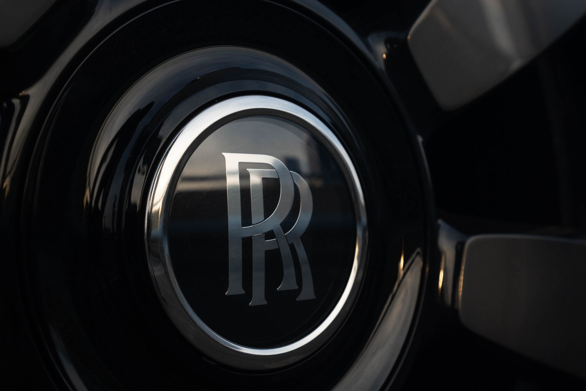 Close-up of a glossy Rolls-Royce hood emblem on a black car.