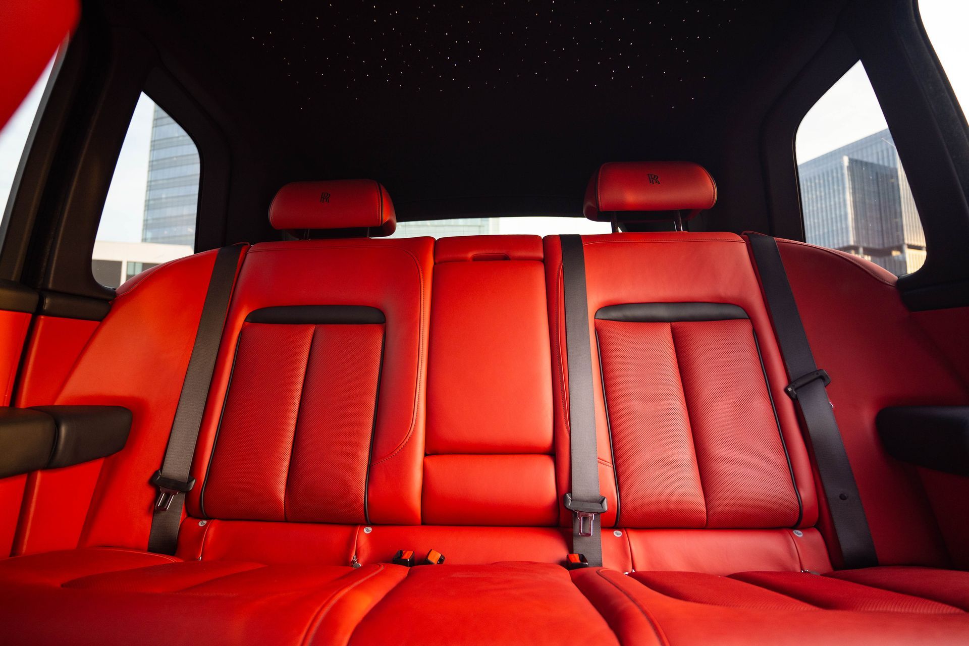Red leather car back seat with headrests and seatbelts, viewed from inside the vehicle.