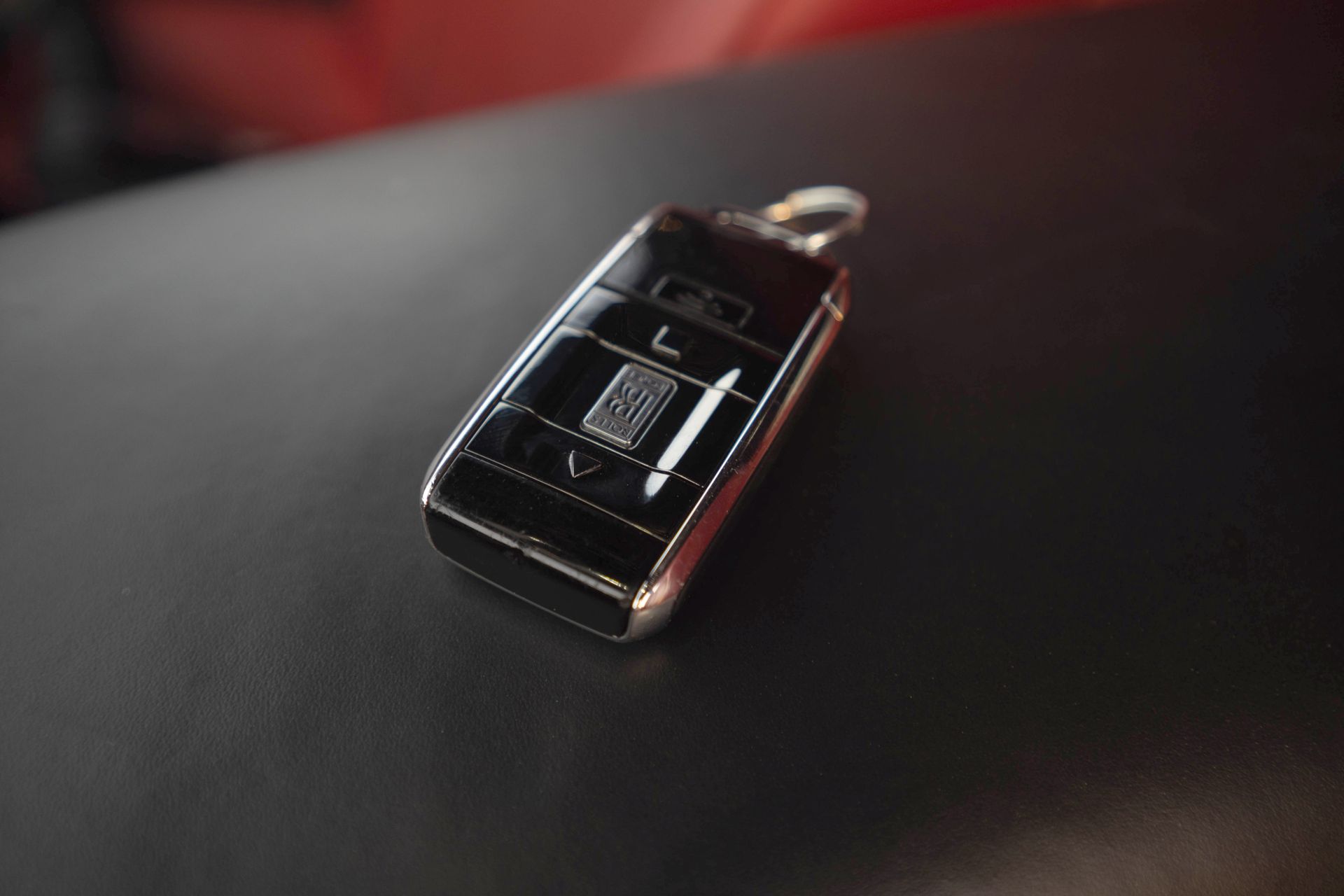 Black car key fob with chrome trim lying on a dark surface, lit by soft red light