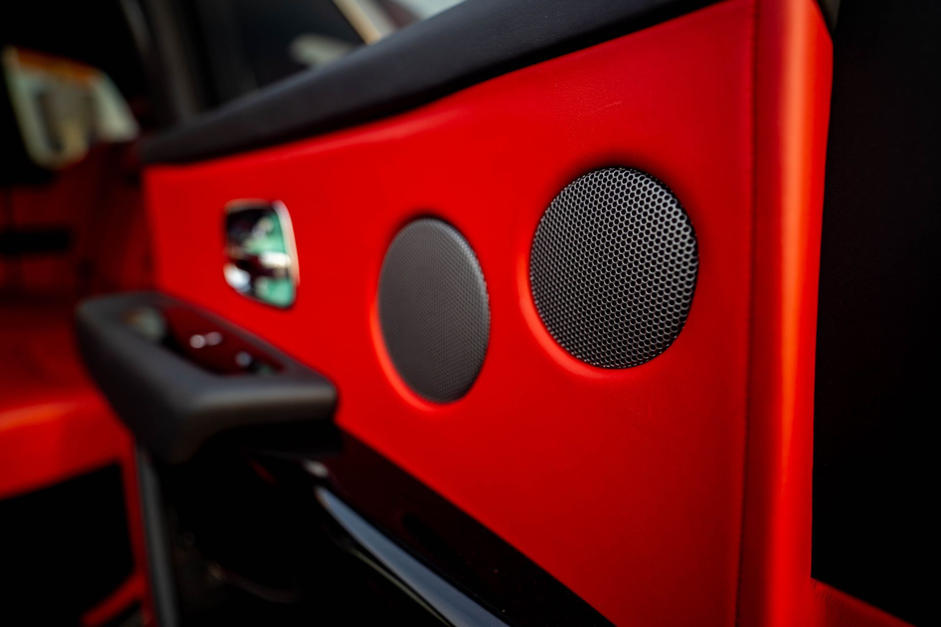 Red car door interior with black speaker grilles and a window control panel