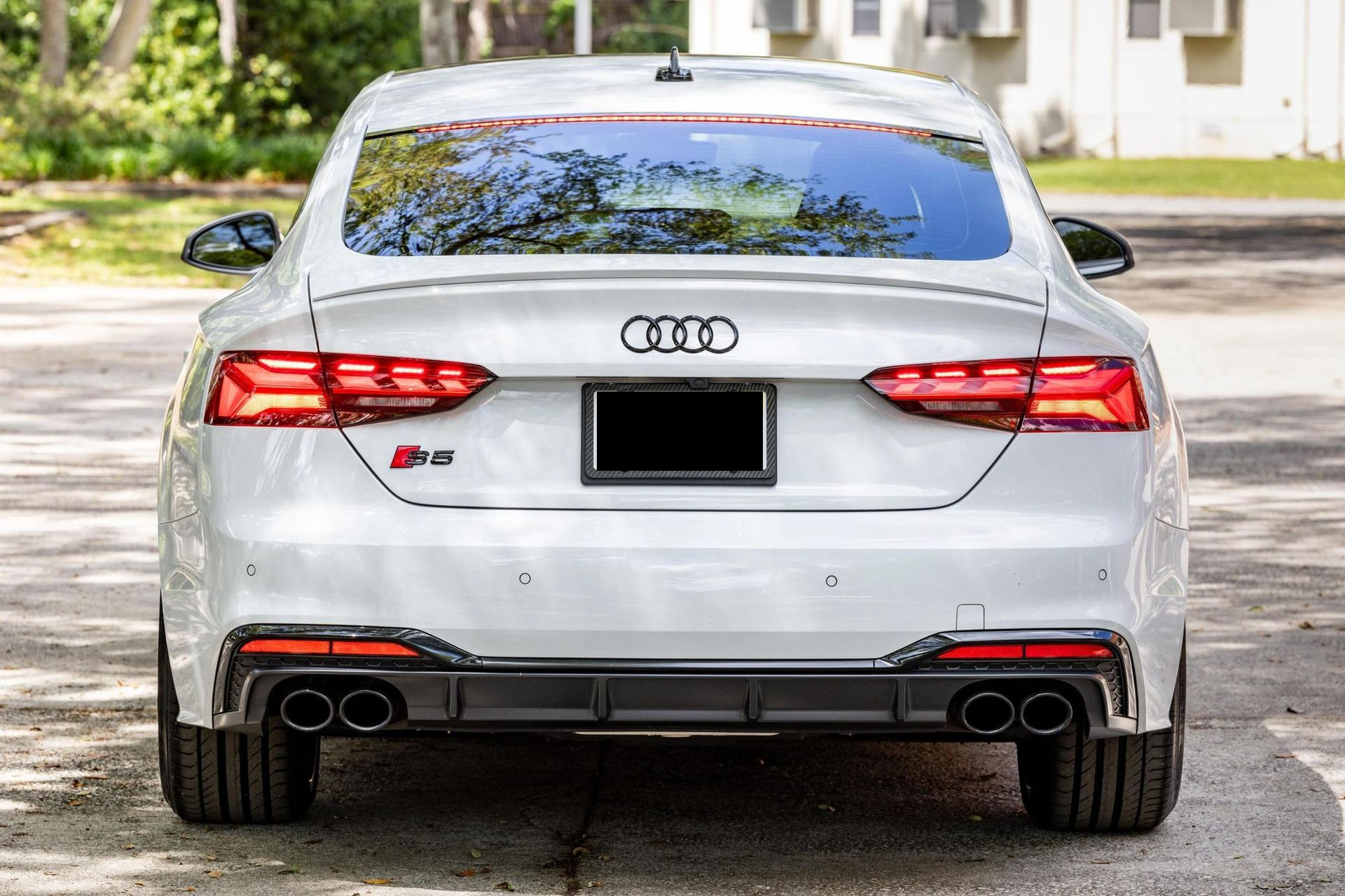 Rear view of a white Audi sedan parked on a driveway, with red taillights and dual exhausts.