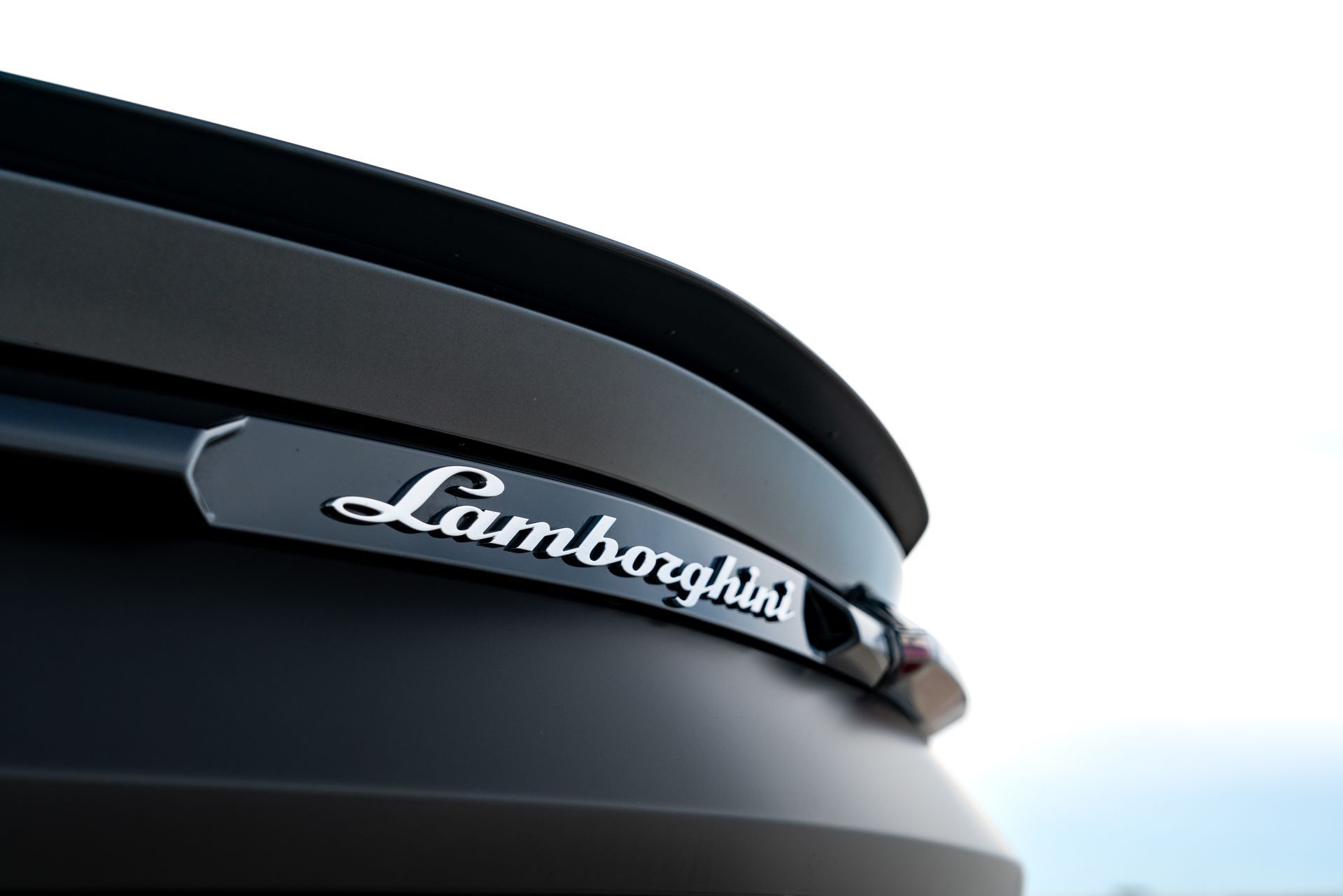Close-up of a Lamborghini rear emblem on a black car against a bright sky