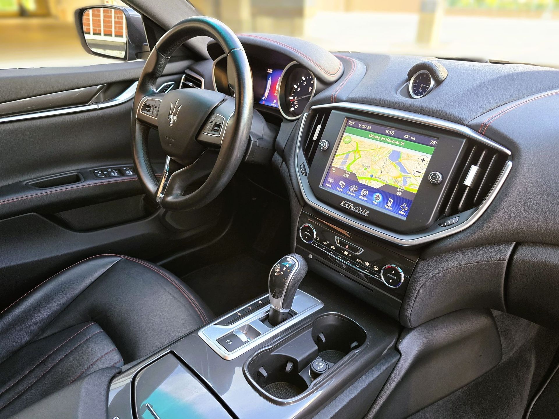 Car interior with black leather seats, dashboard screen, steering wheel, and center console.