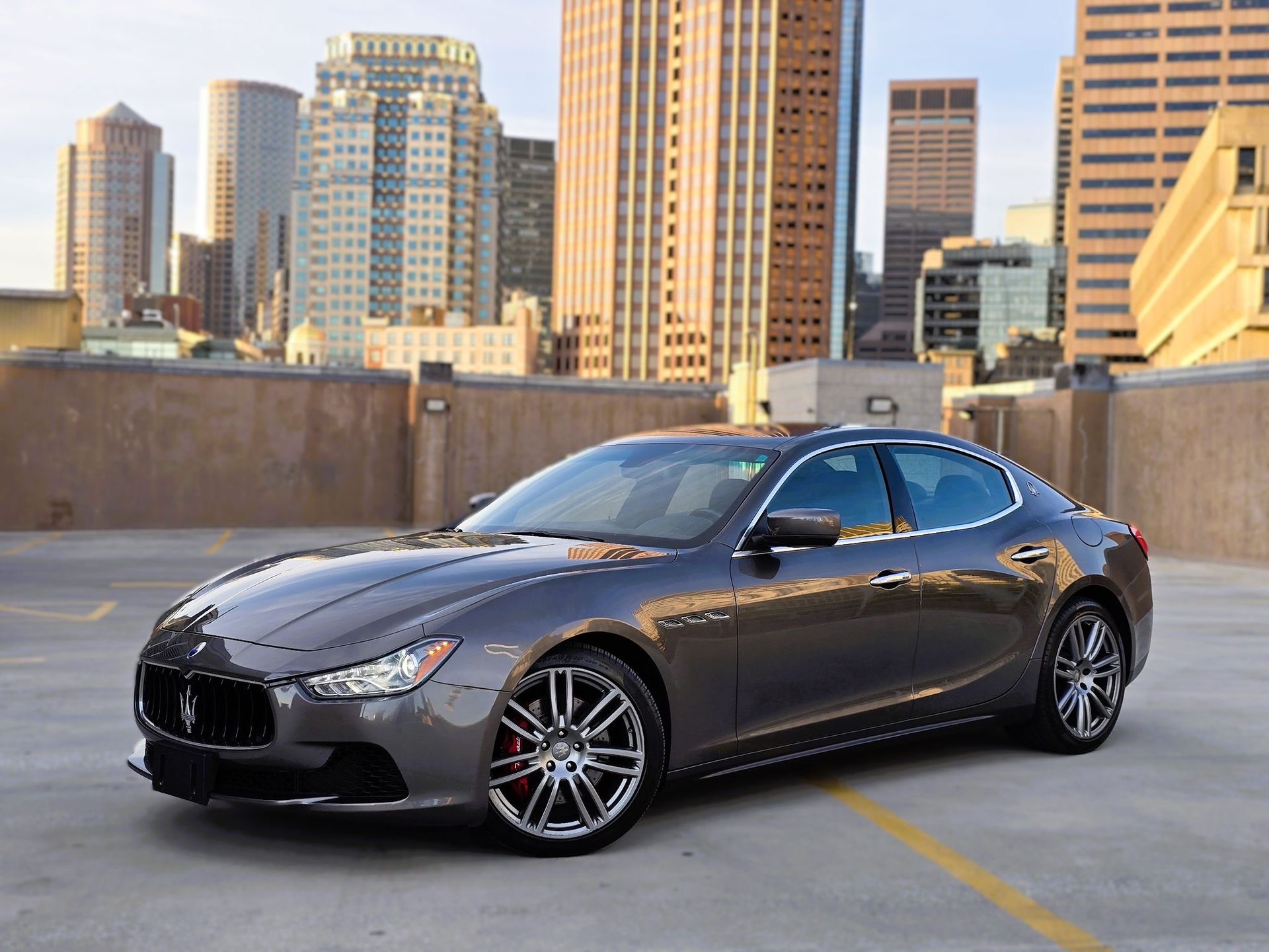 Dark gray sports sedan parked on a rooftop lot with city buildings in the background