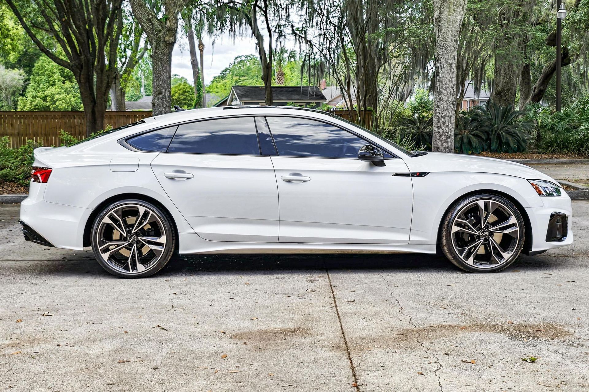 White sports sedan with black-and-gold rims parked on a driveway surrounded by trees