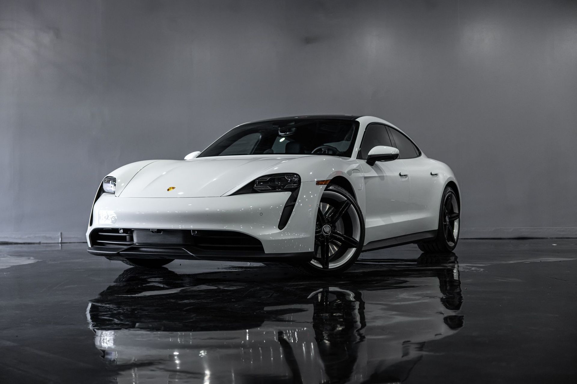 White Porsche Taycan electric car on a reflective surface in a studio.