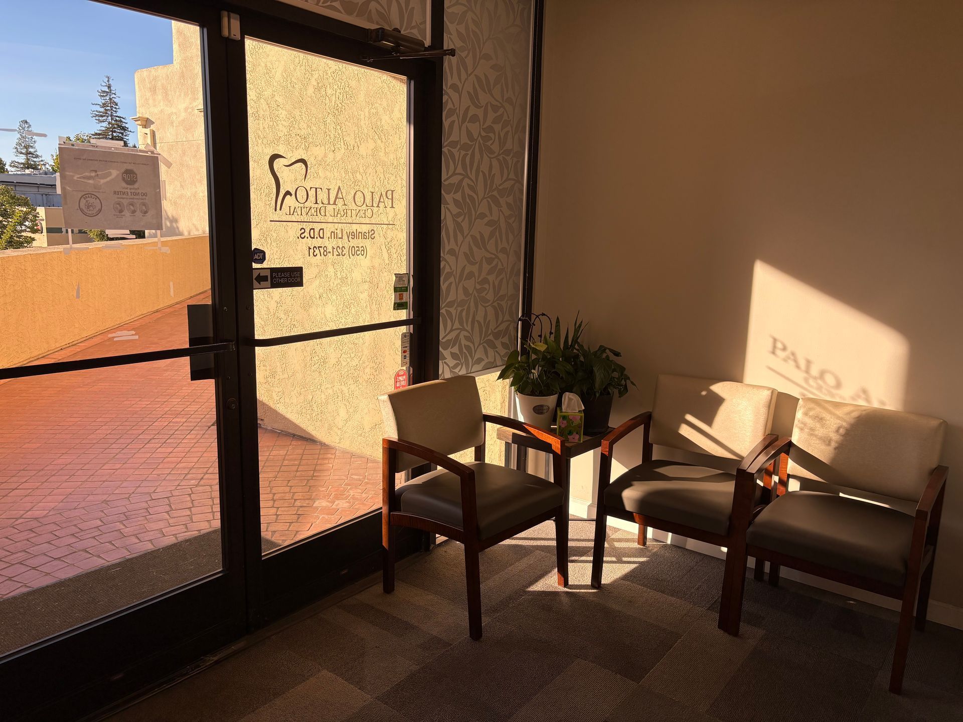 Sunlit lobby with glass door, two chairs, and a potted plant by the window.