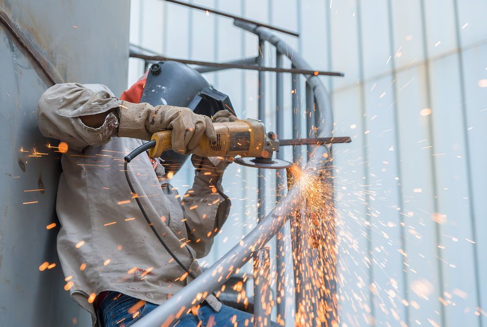 A Man Is Cutting A Metal Railing With A Grinder — Keystone Engineering Sheet Metal Industries in Noosaville, QLD