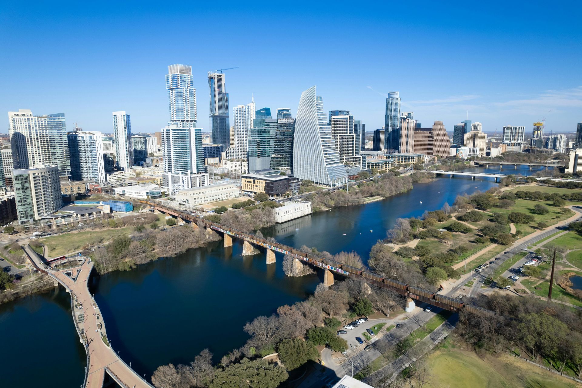 Aerial view of a city skyline with a river, bridges, and green parkland on a clear day