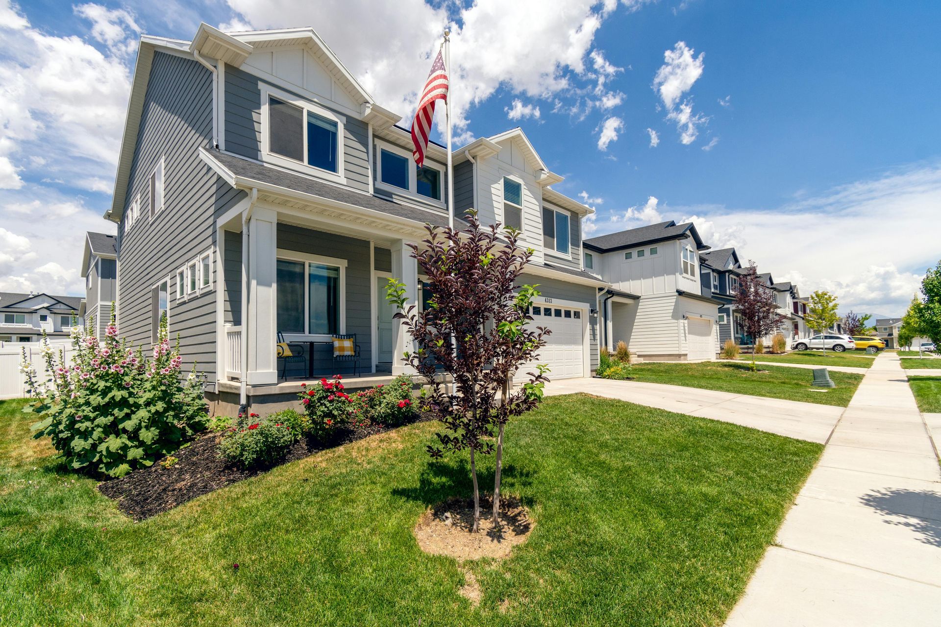 Suburban townhouse with gray siding, front lawn, porch, and American flag on a sunny day