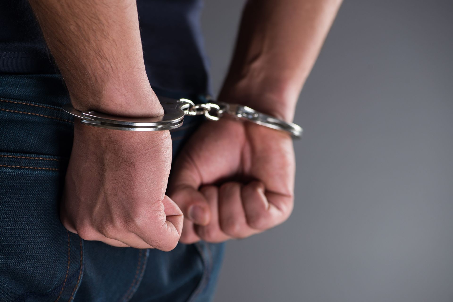 Handcuffed hands behind a person's back against a dark background