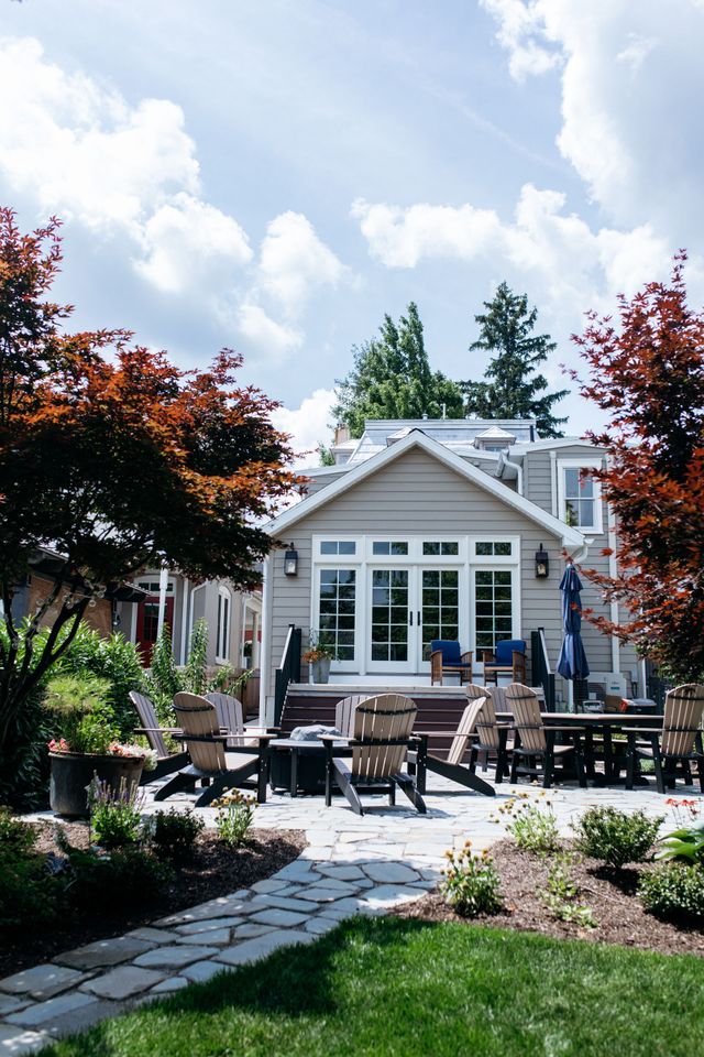Backyard patio with outdoor seating, stone path, and a small house framed by trees and flowers