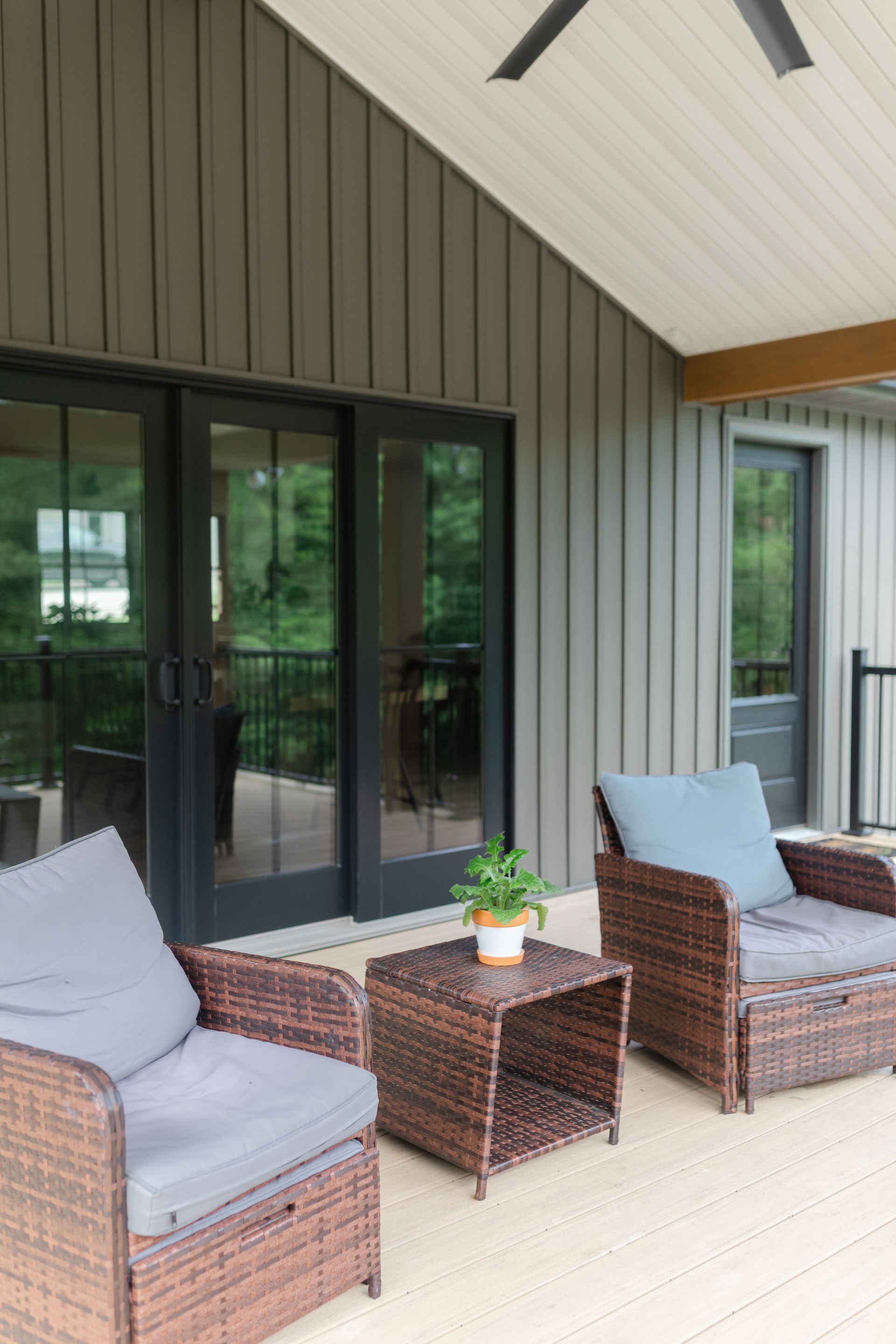 Covered patio with wicker chairs, gray cushions, and a small table by glass sliding doors.