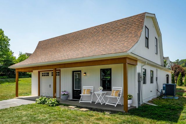White farmhouse with tan roof and porch seating in a sunny grassy yard