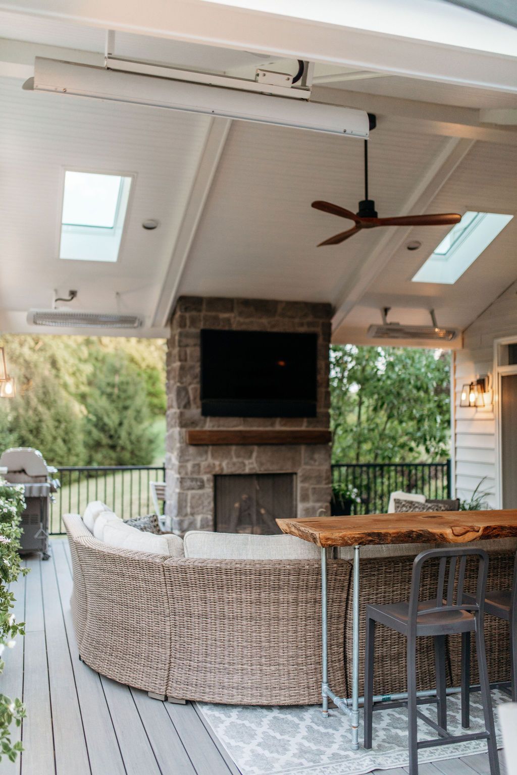 Covered patio with wicker sectional, bar stools, TV above fireplace, skylights, and ceiling fan