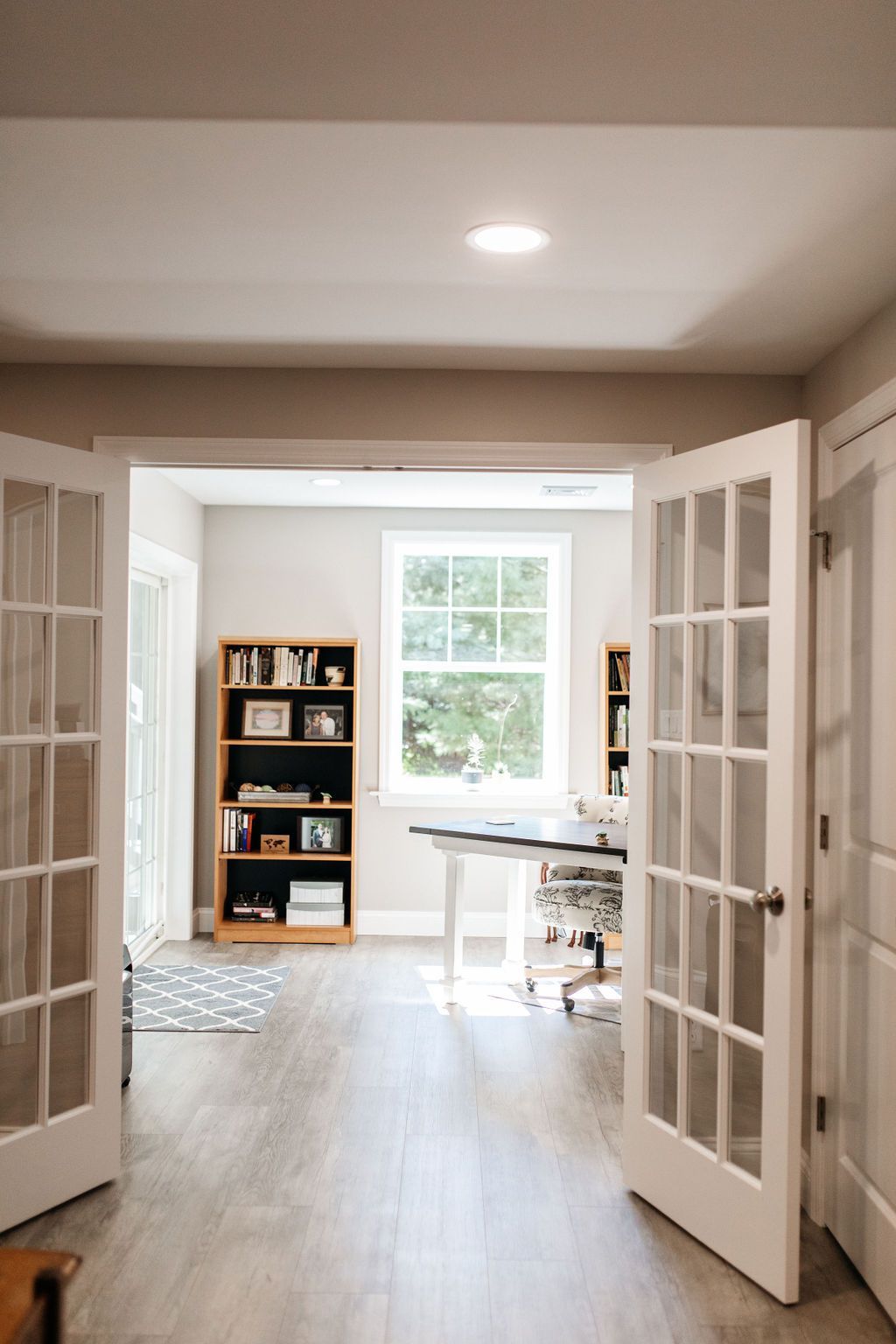 Bright home office with open French doors, desk, bookshelf, and window light.