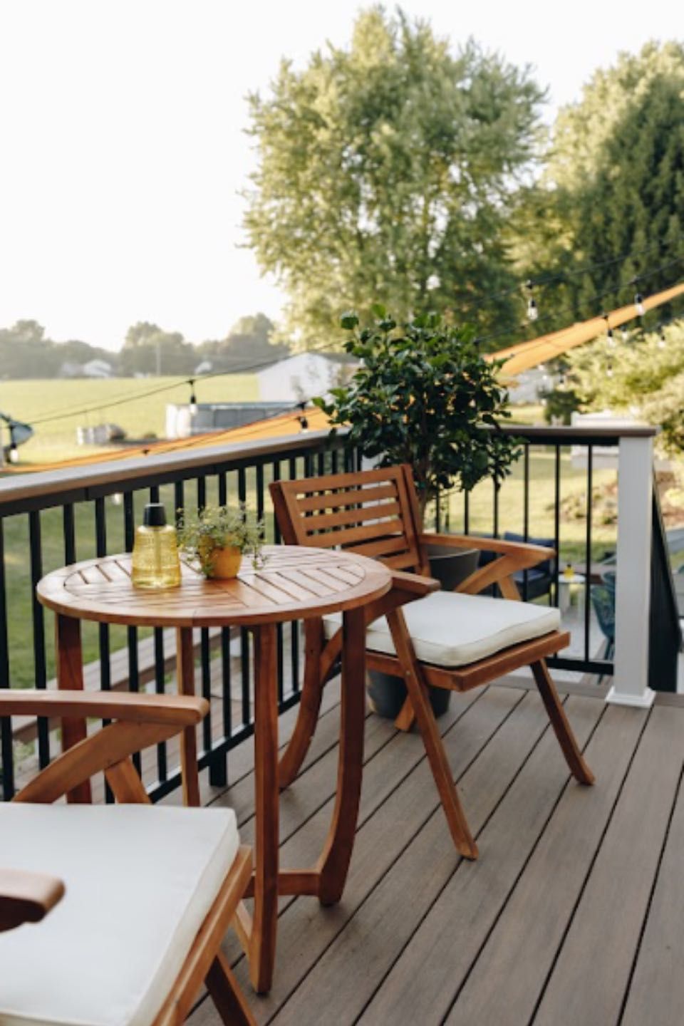 Patio deck with wooden table, chairs, and drinks overlooking a grassy yard and trees
