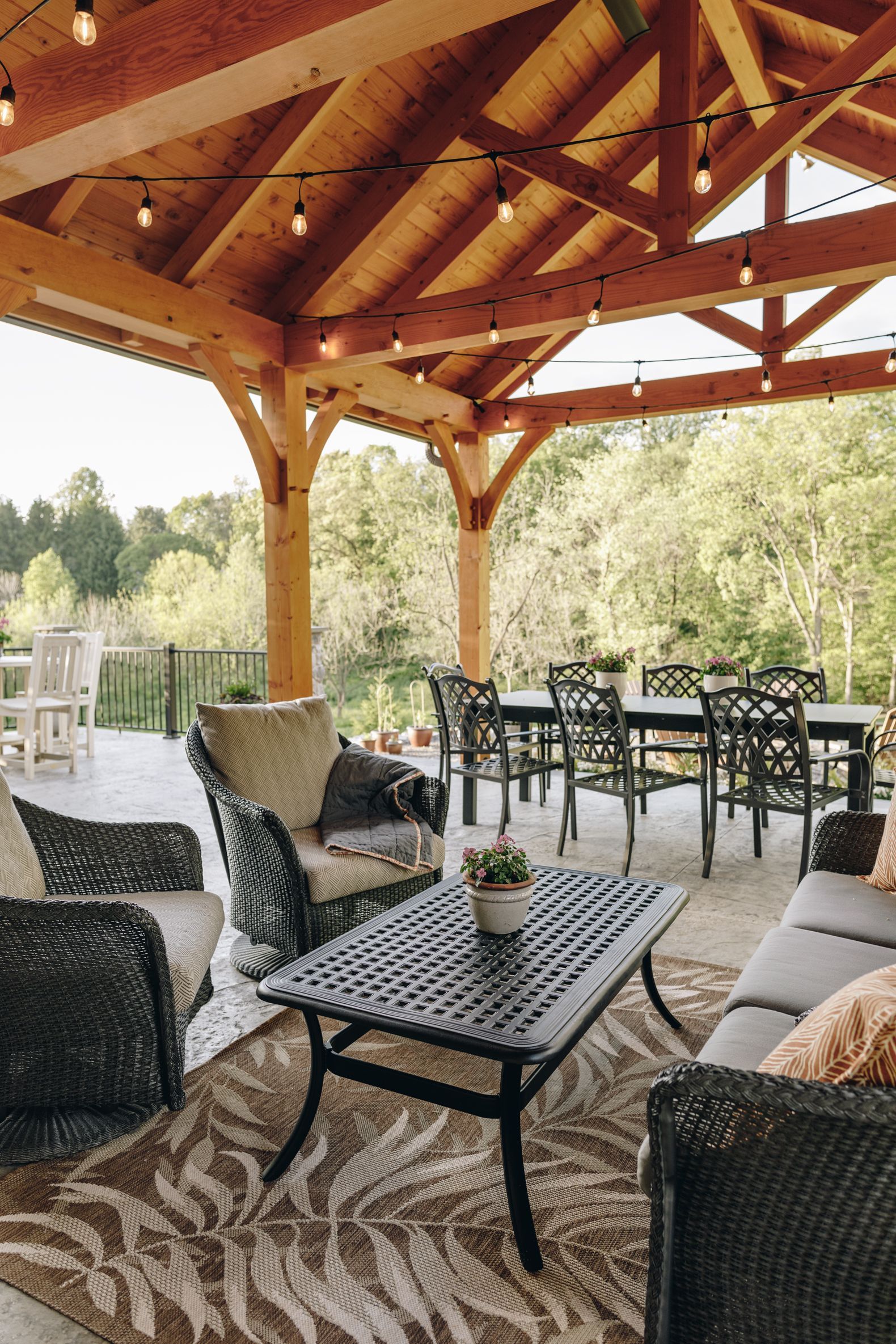 Covered outdoor patio with wicker seating, black metal tables, and a wooden pavilion overlooking greenery