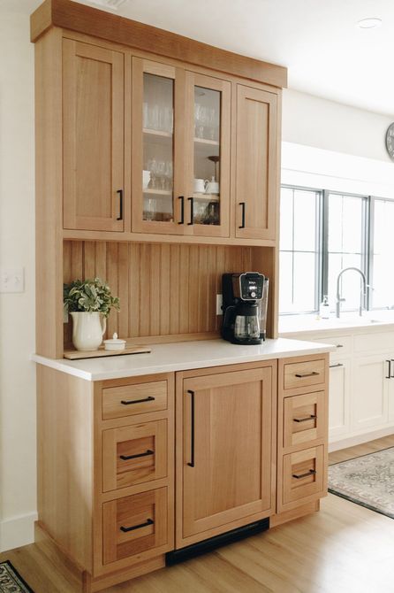 Wooden kitchen cabinet with white countertop, coffee maker, and potted plant in a bright room