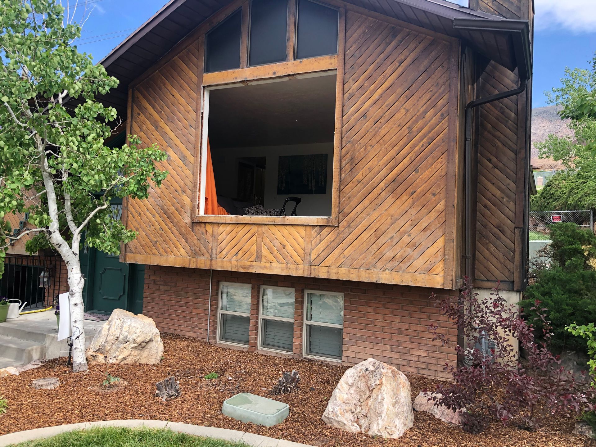 House exterior with wood siding, large window, brick base, and landscaping.