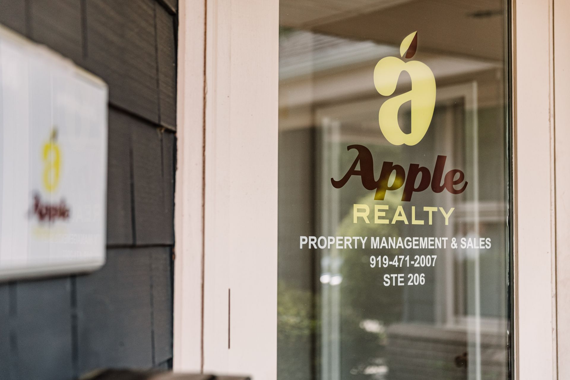Apple Realty office door with gold signage showing the company name, services, phone number, and suite 208.