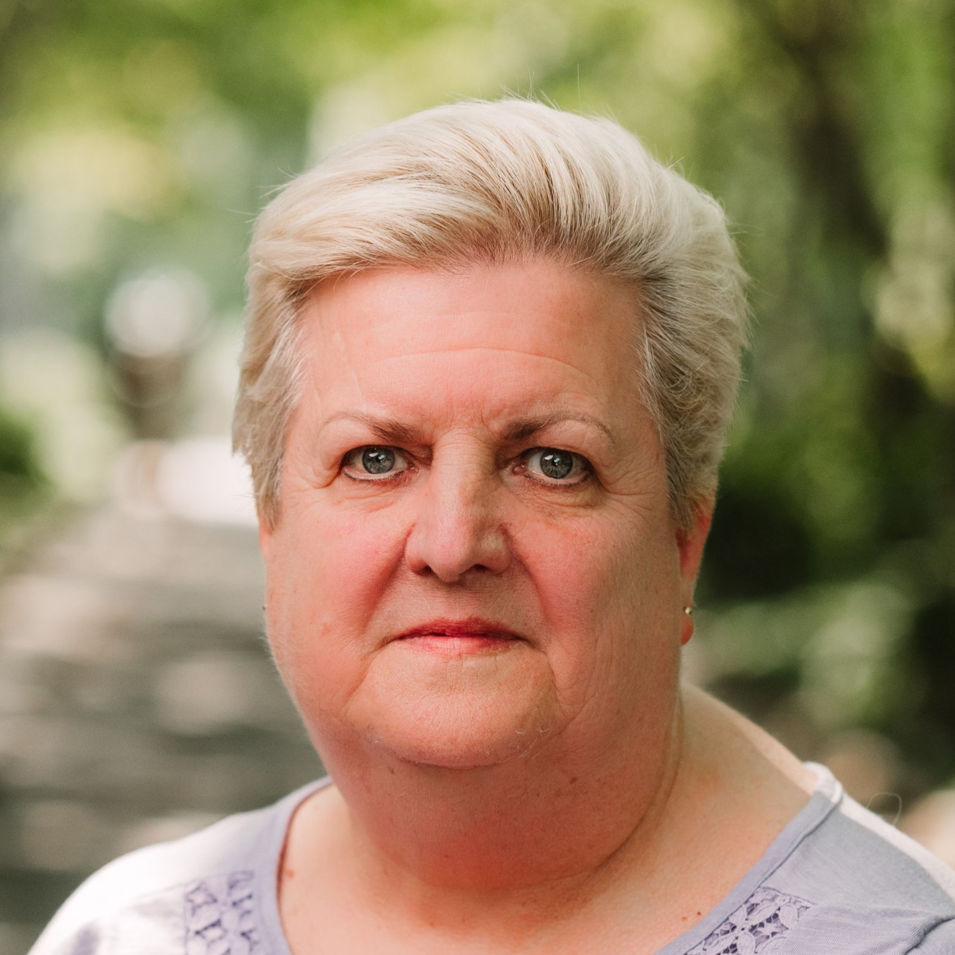 A close-up portrait of a person with short blonde hair against a soft-focus, natural green background.